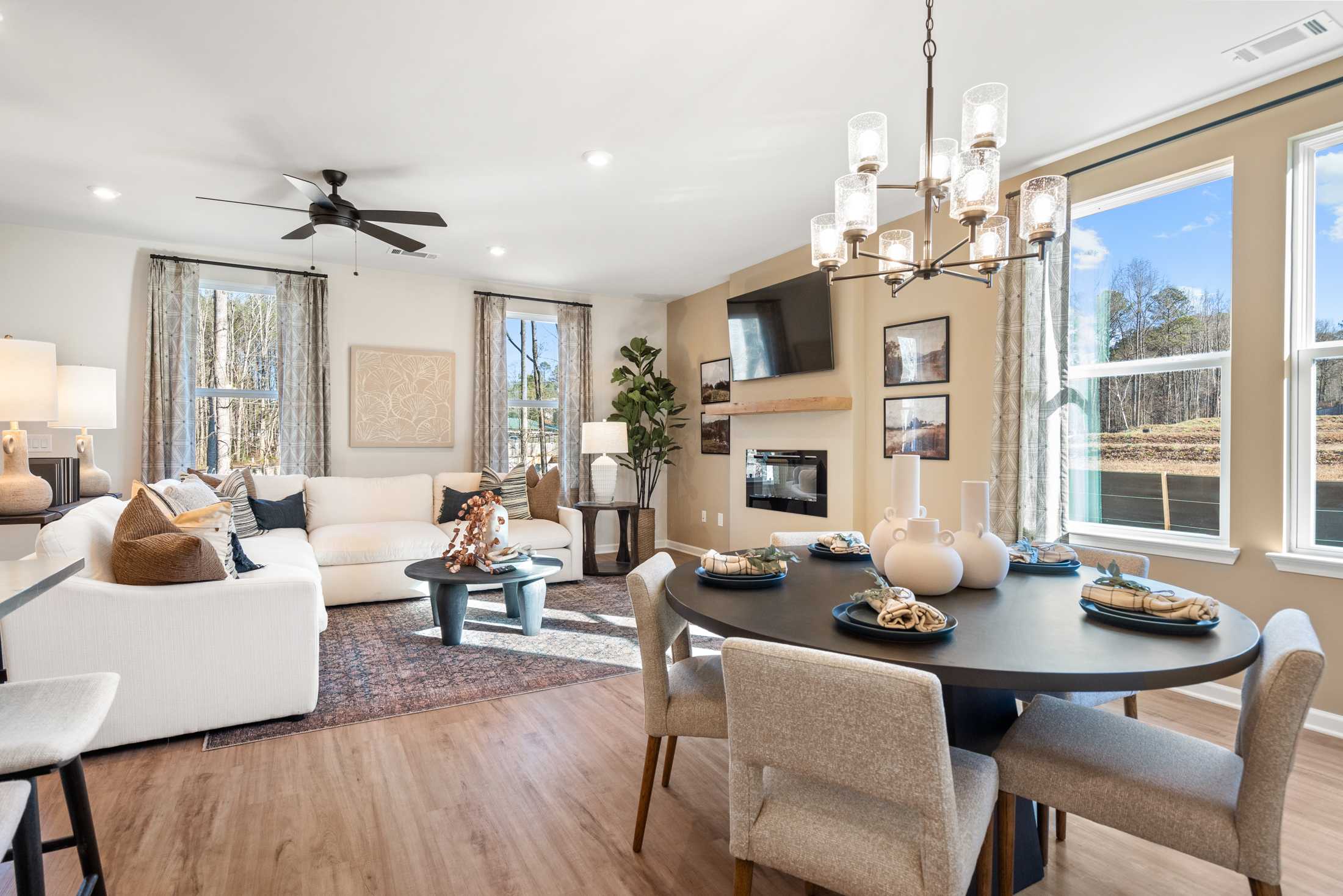 Open-concept living and dining area in The Marion A by Davidson Homes featuring white sofa, round table, fireplace, chandelier, and large windows with scenic views