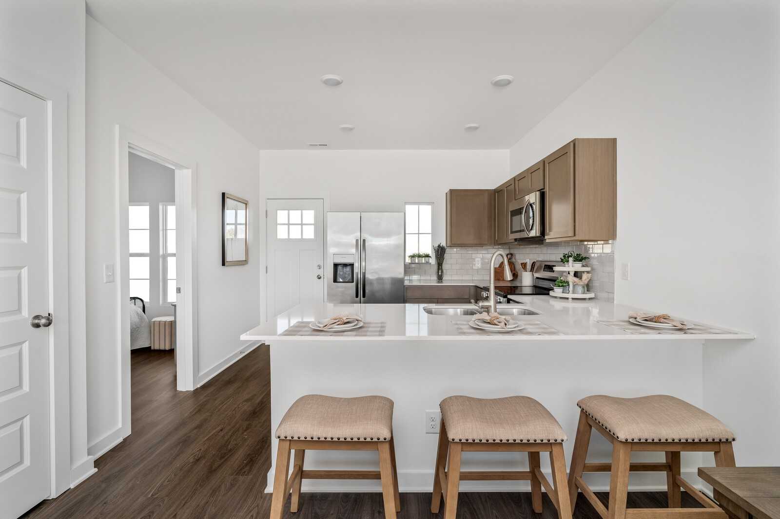 Modern open-concept kitchen with stainless appliances, beige cabinets, and island bar stools in Davidson Homes The Cumberland A, Gallatin, TN