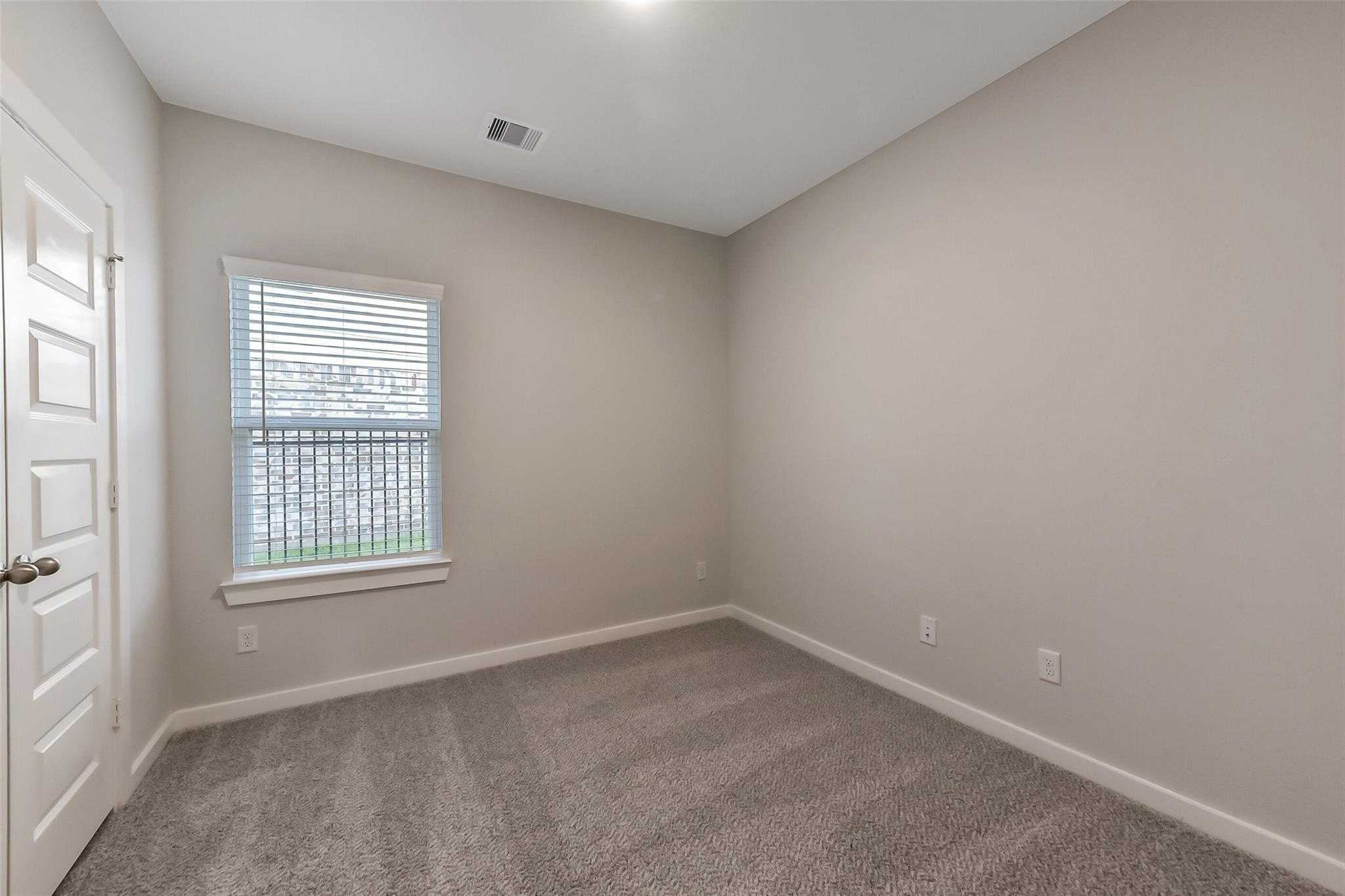 Empty secondary bedroom featuring beige walls, berber carpet, and window blinds in Davidson Homes The Laguna B, Sunterra, Katy, Texas