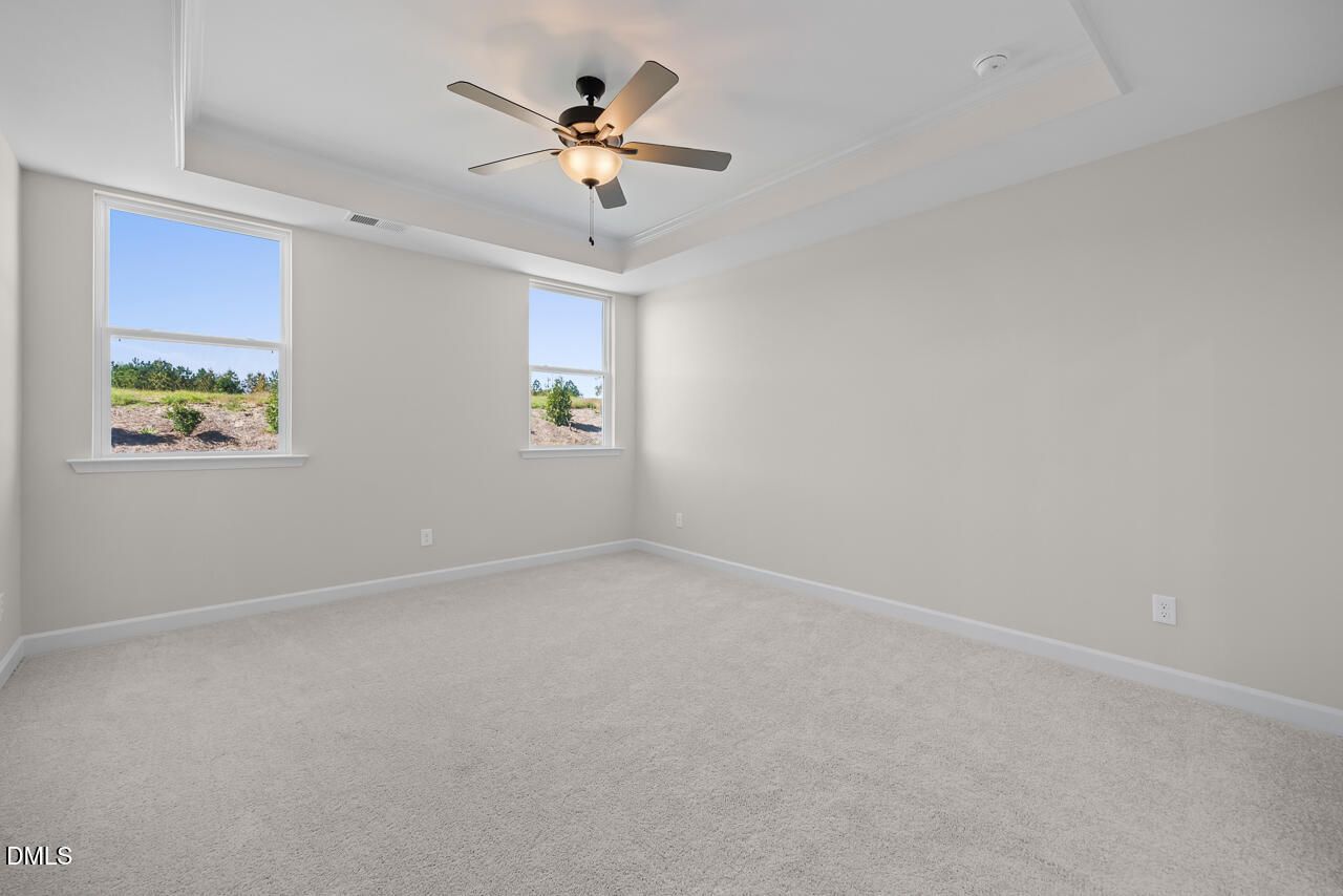 Bright spacious bedroom with tray ceiling, ceiling fan, carpet flooring, and double windows in Davidson Homes Ashport M, Wendell NC