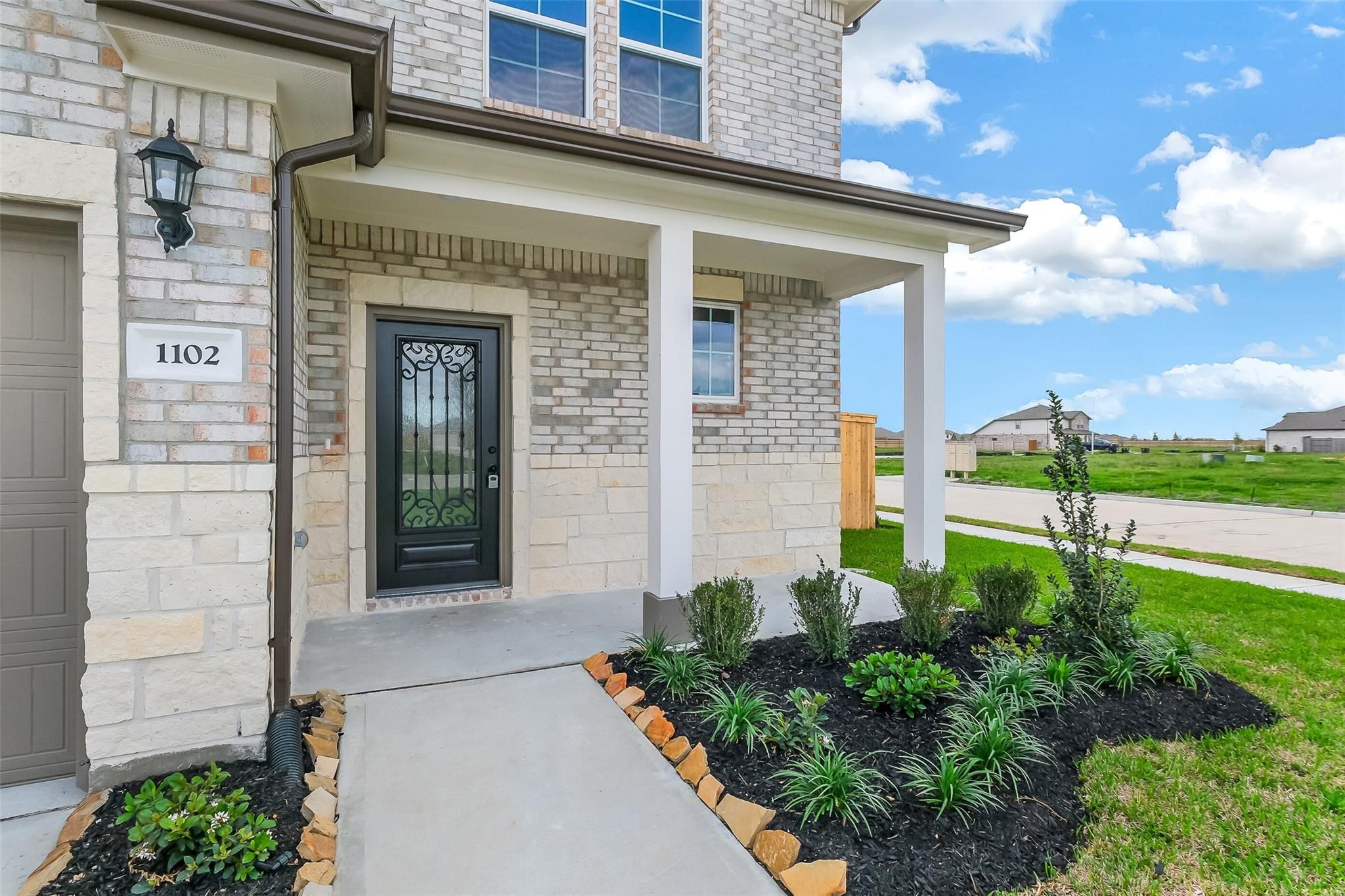 Modern two-story brick home facade with two-car garage, wrought iron entry door at 1102, covered porch, and landscaped walkway in Emberly, Beasley, Texas
