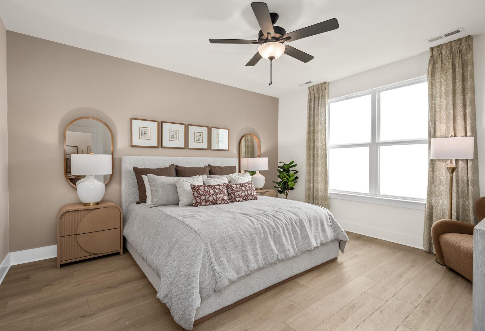 Serene main-floor master suite in The Ridgeport by Davidson Homes featuring neutral bedding, large windows, and ceiling fan