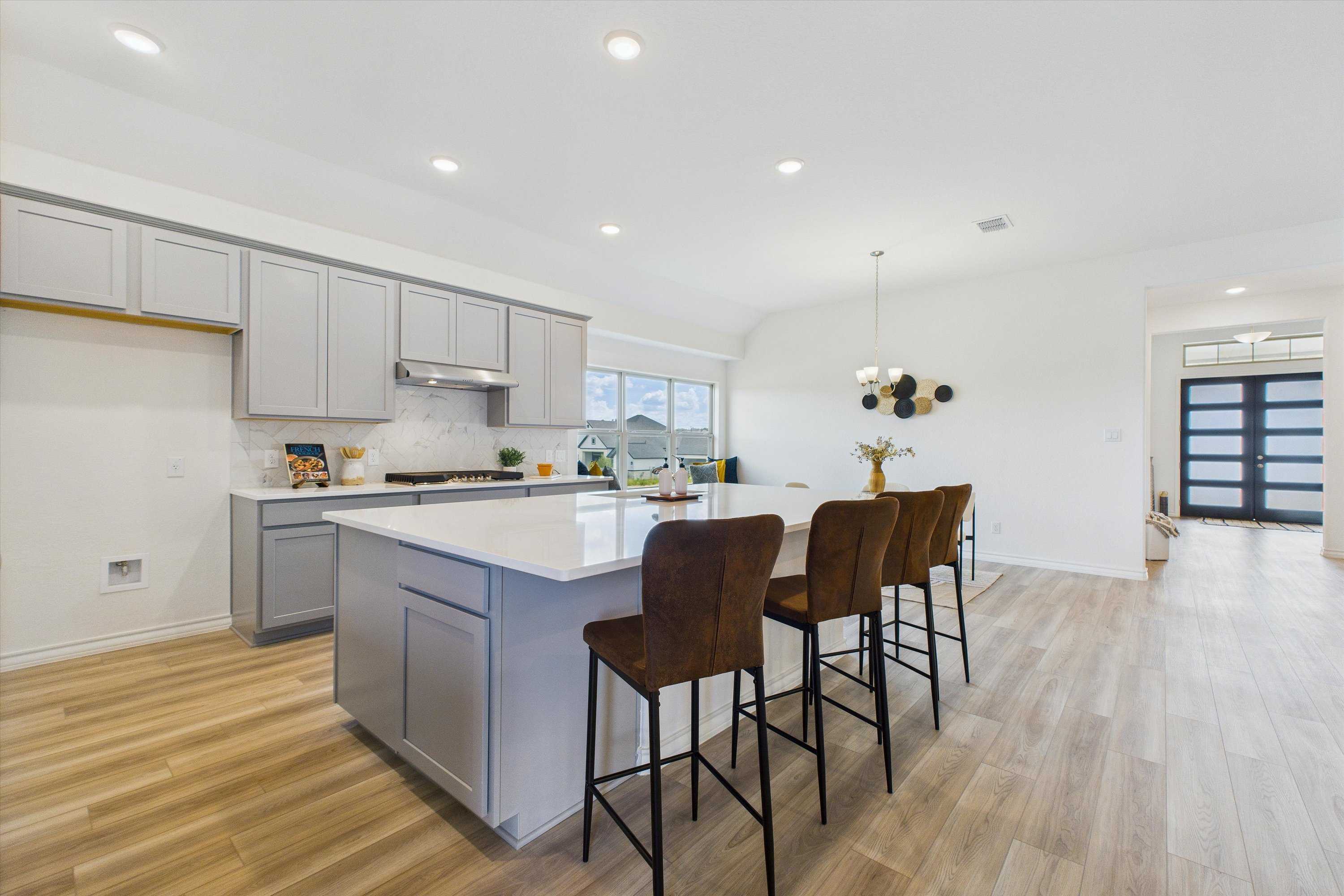 Modern kitchen featuring gray shaker cabinets, white quartz island, and upholstered bar stools in Davidson Homes The Summerlin C, Castroville, TX