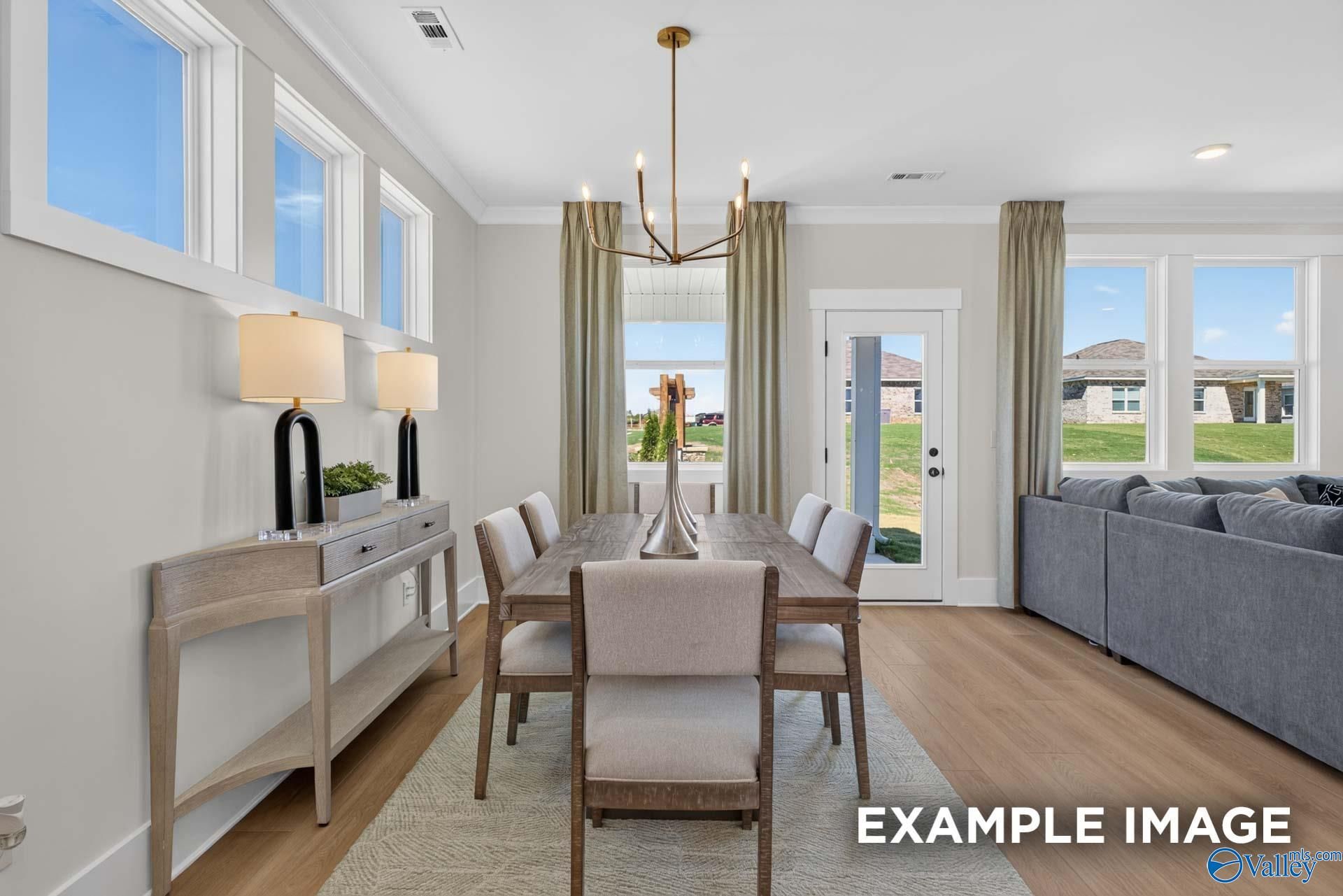 Bright dining area with wood table, brass chandelier, and open living room in Davidson Homes Ashport K, Hazel Green, Alabama