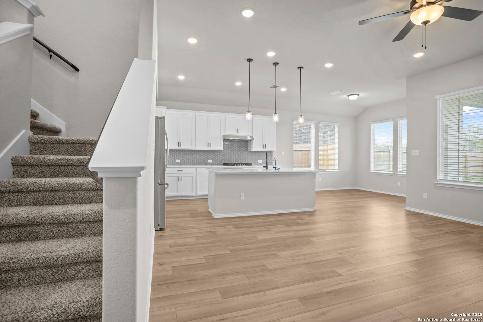 Open-concept kitchen with white cabinets, stainless appliances, island, and adjacent living space in Davidson Homes The Sequoia A, Converse, Texas