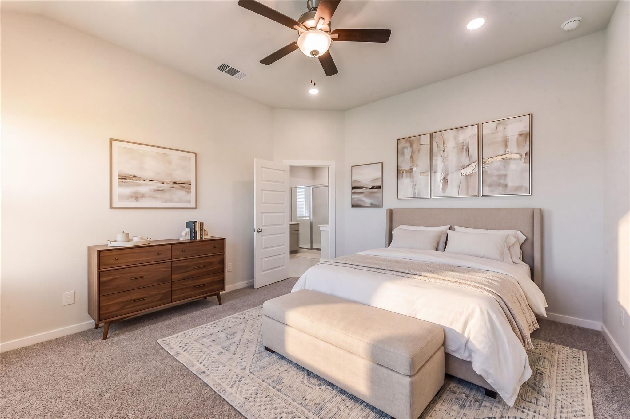 Elegant master bedroom with king bed, wooden dresser, beige ottoman, abstract art, ceiling fan, and en-suite bath in Davidson Homes The Costa C, Dayton, Texas