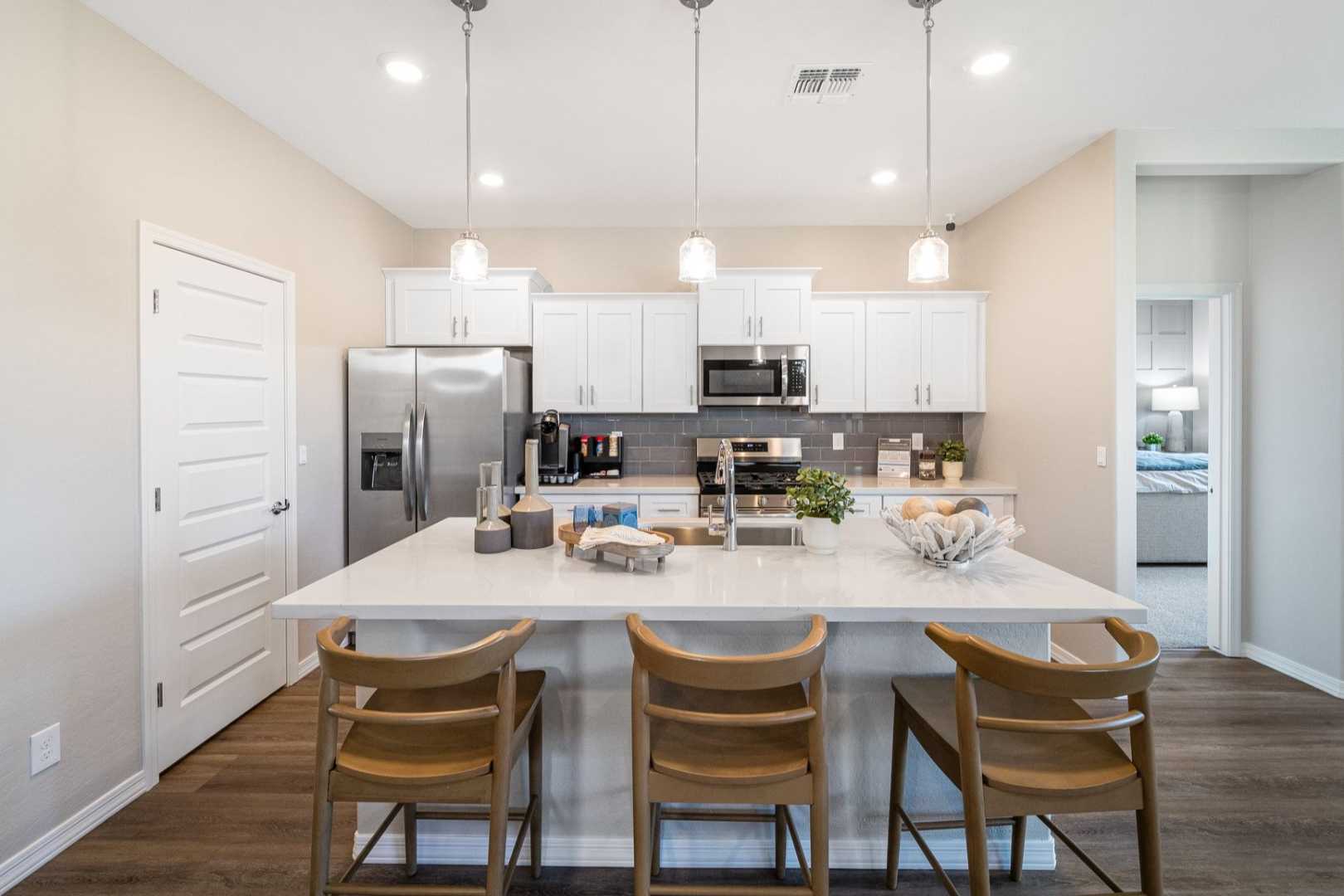 Modern kitchen in The Newport B by Davidson Homes featuring white shaker cabinets, large island with wooden stools, stainless appliances, and open layout