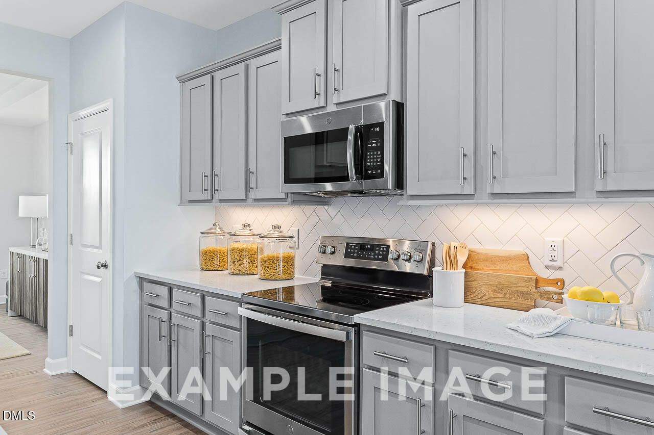 Modern kitchen with gray shaker cabinets, stainless appliances, and herringbone backsplash in Davidson Homes The Ash C plan