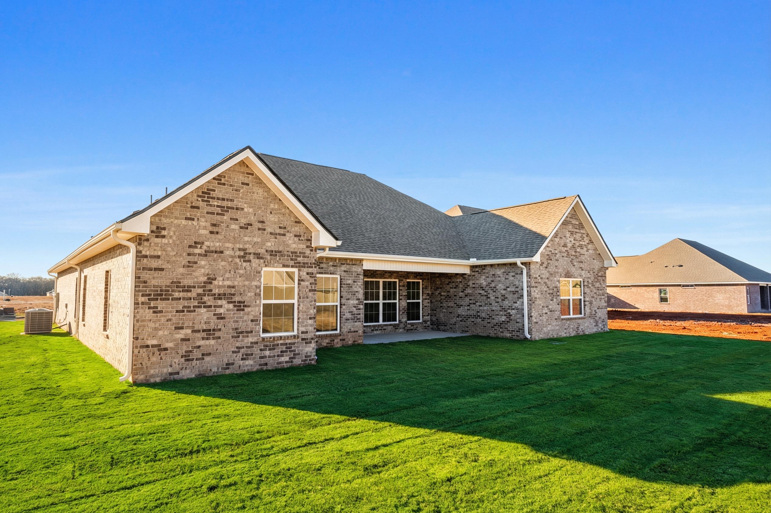 Side view of The Valencia single-story home with brick exterior, covered patio, large windows, and lush green lawn