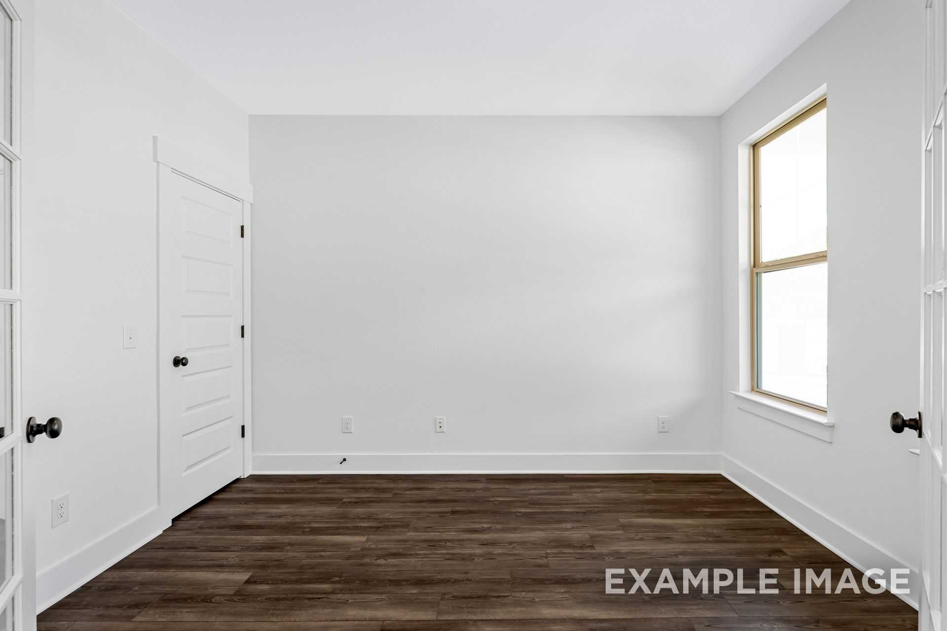 Spacious empty master bedroom in The Logan B with white walls, hardwood floors, large window, and double doors