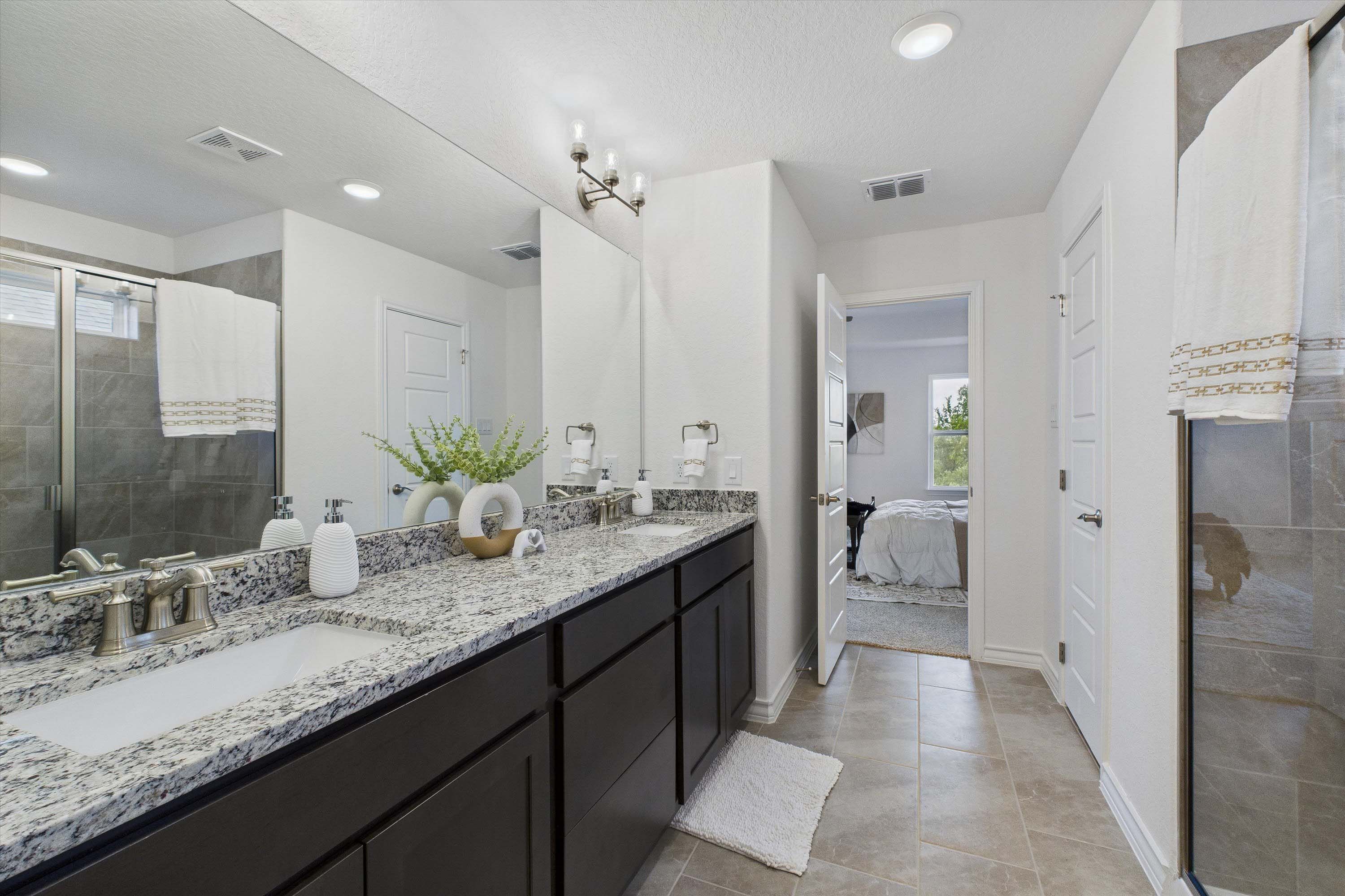 Modern master bathroom in The Danbury featuring dual vanity, granite countertops, and tiled walk-in shower.