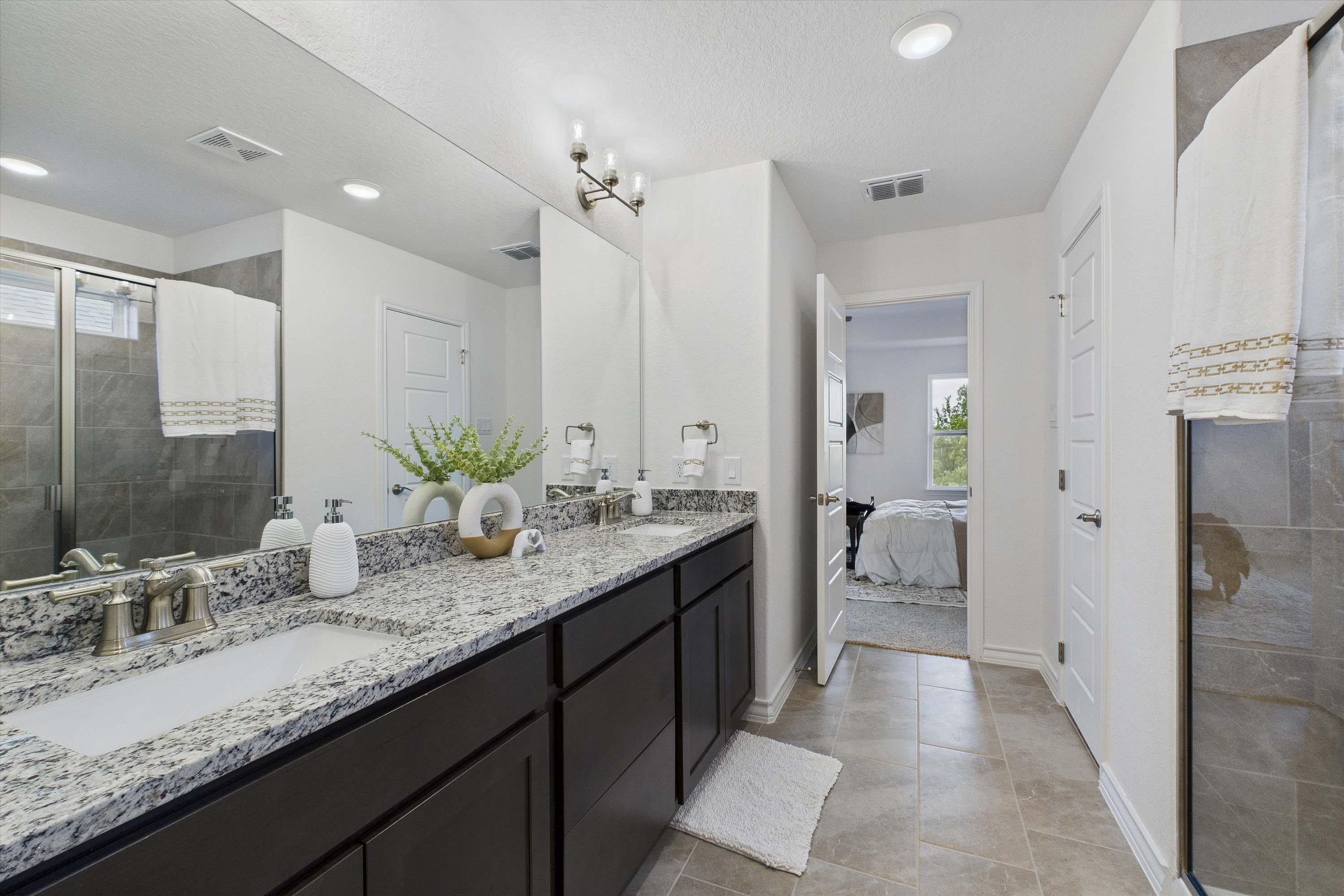 Modern master bathroom in The Danbury featuring dual vanity, granite countertops, and tiled walk-in shower.