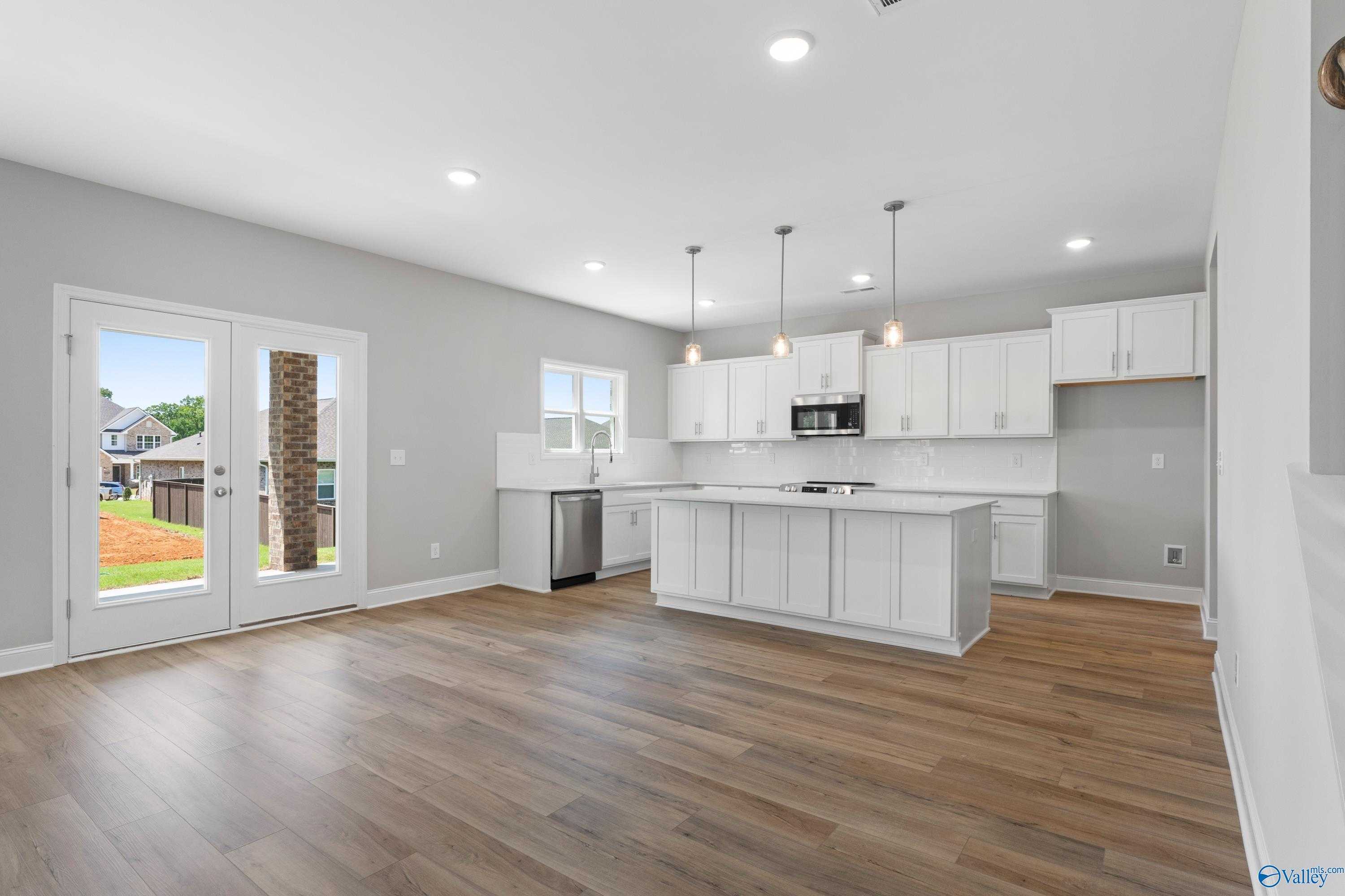 Spacious open-concept kitchen with white cabinets, large island, stainless appliances, and French doors to backyard patio in Davidson Homes Chelsea B, New Market, AL