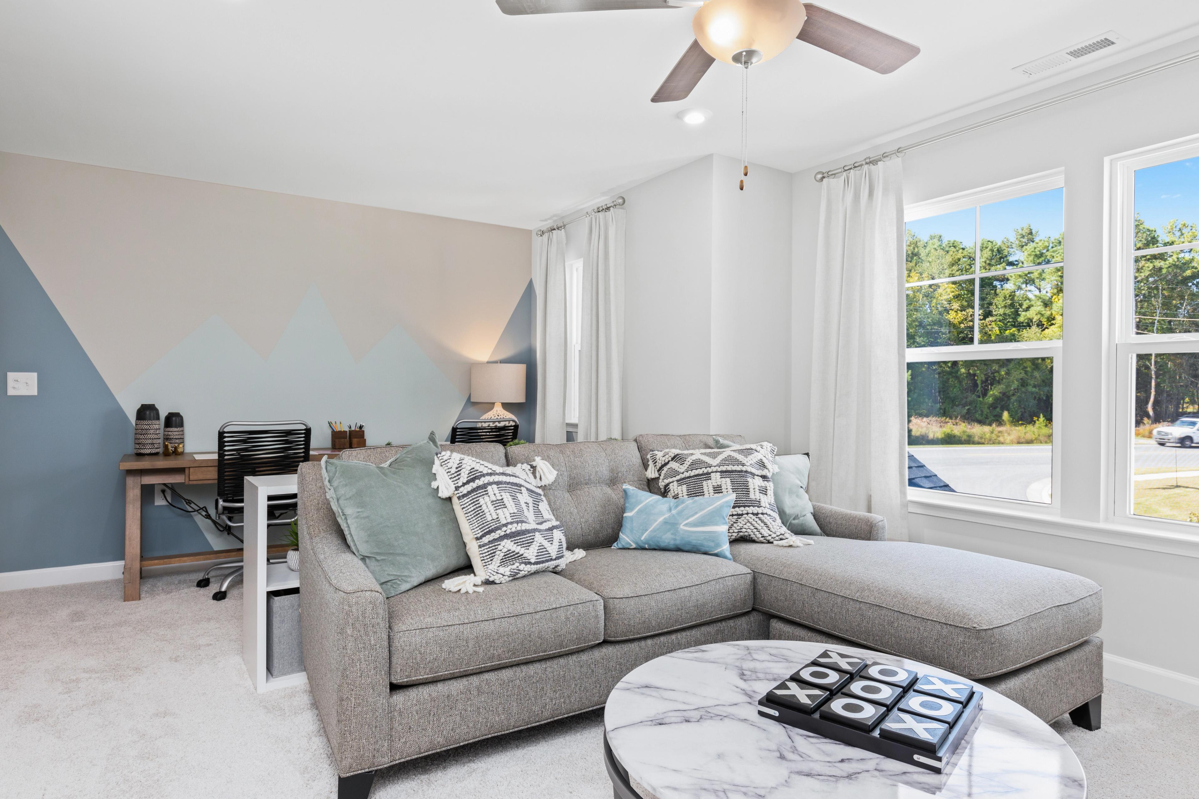 Cozy living room at Enclave at Belmont in Belmont NC with gray L-shaped sectional sofa, geometric accent wall, ceiling fan, corner desk, and large windows