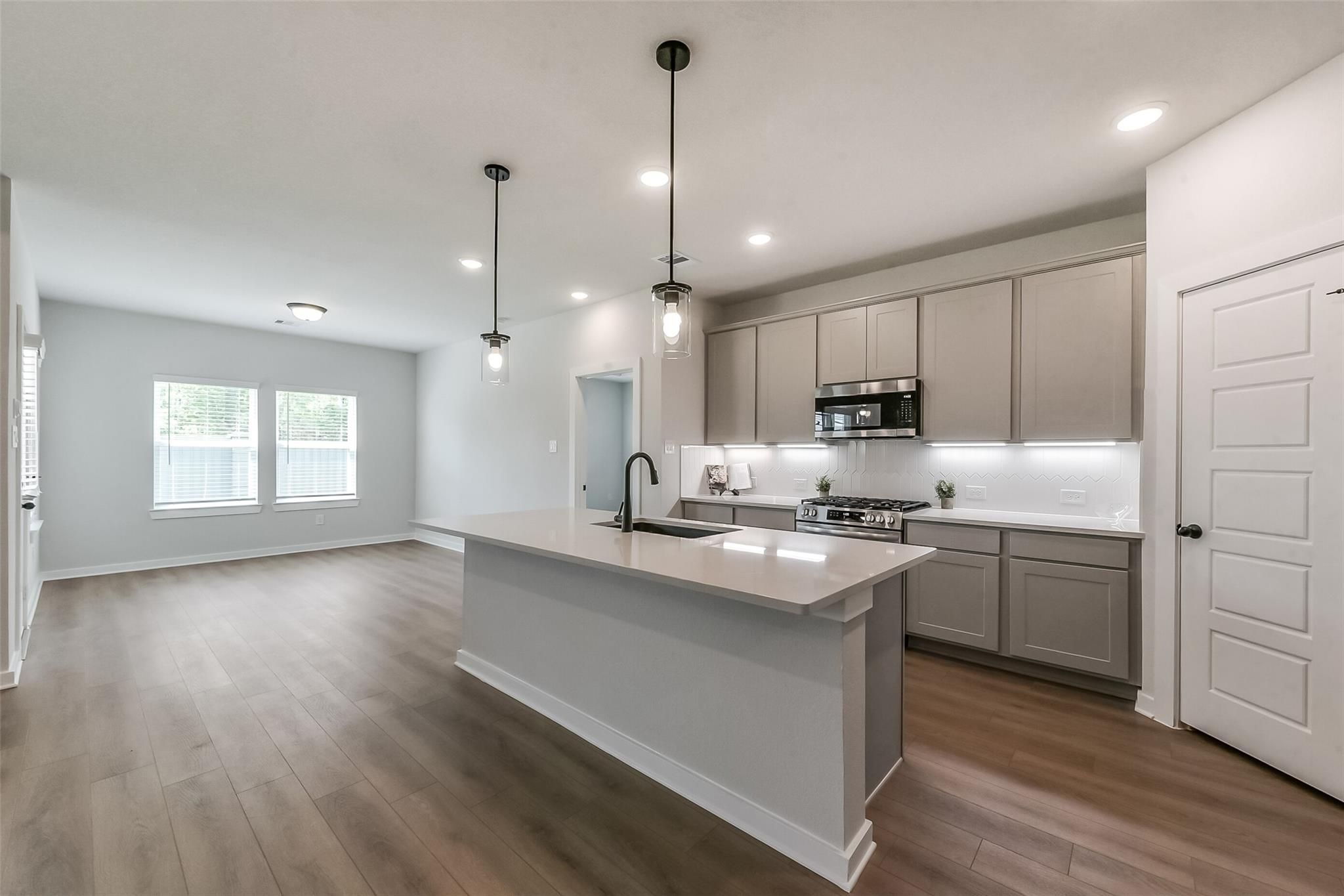 Modern kitchen with quartz island, gray cabinets, stainless appliances in The Everett C, Davidson Homes, Crosby, TX
