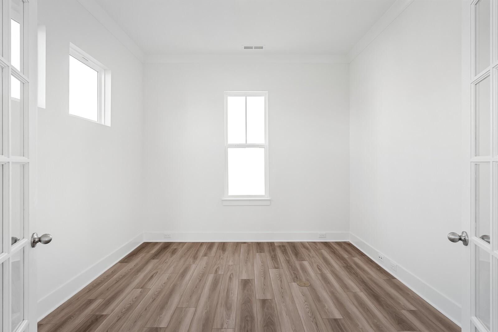 Bright empty room with hardwood floors, white walls, French doors, and large windows in The Alston A floor plan, Murfreesboro, TN