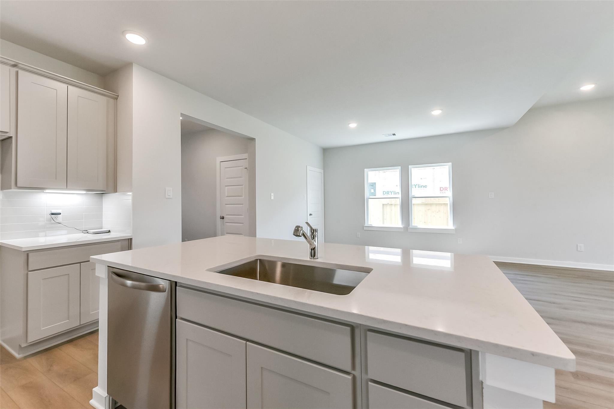 Open-concept kitchen with quartz island, stainless sink and dishwasher, gray cabinets in Davidson Homes Tierra C 4-bedroom home, Dayton TX