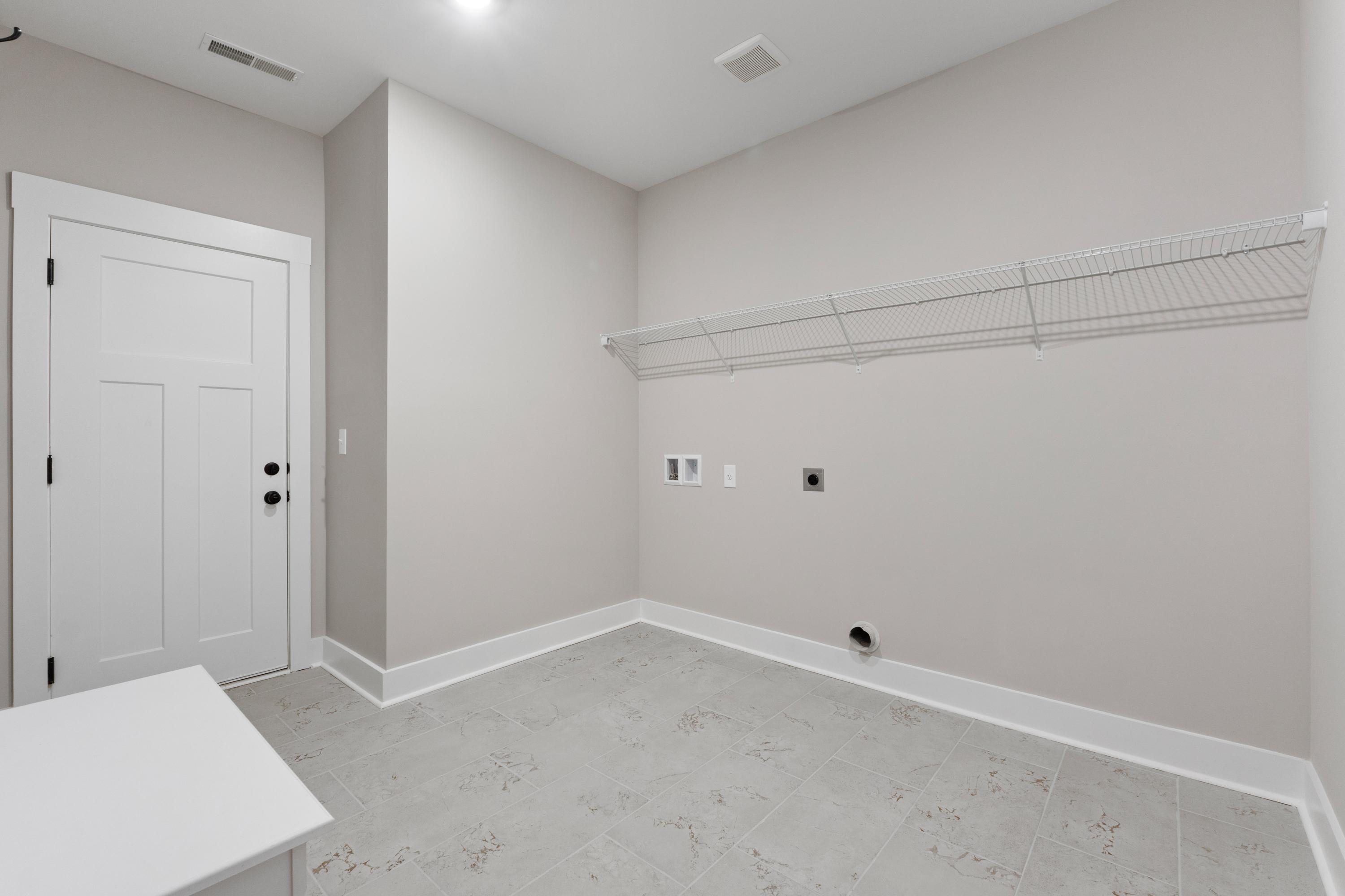 Spacious laundry room in The Oxford home by Evermore Homes with built-in wire shelving, washer dryer hookups, and neutral gray walls flooring