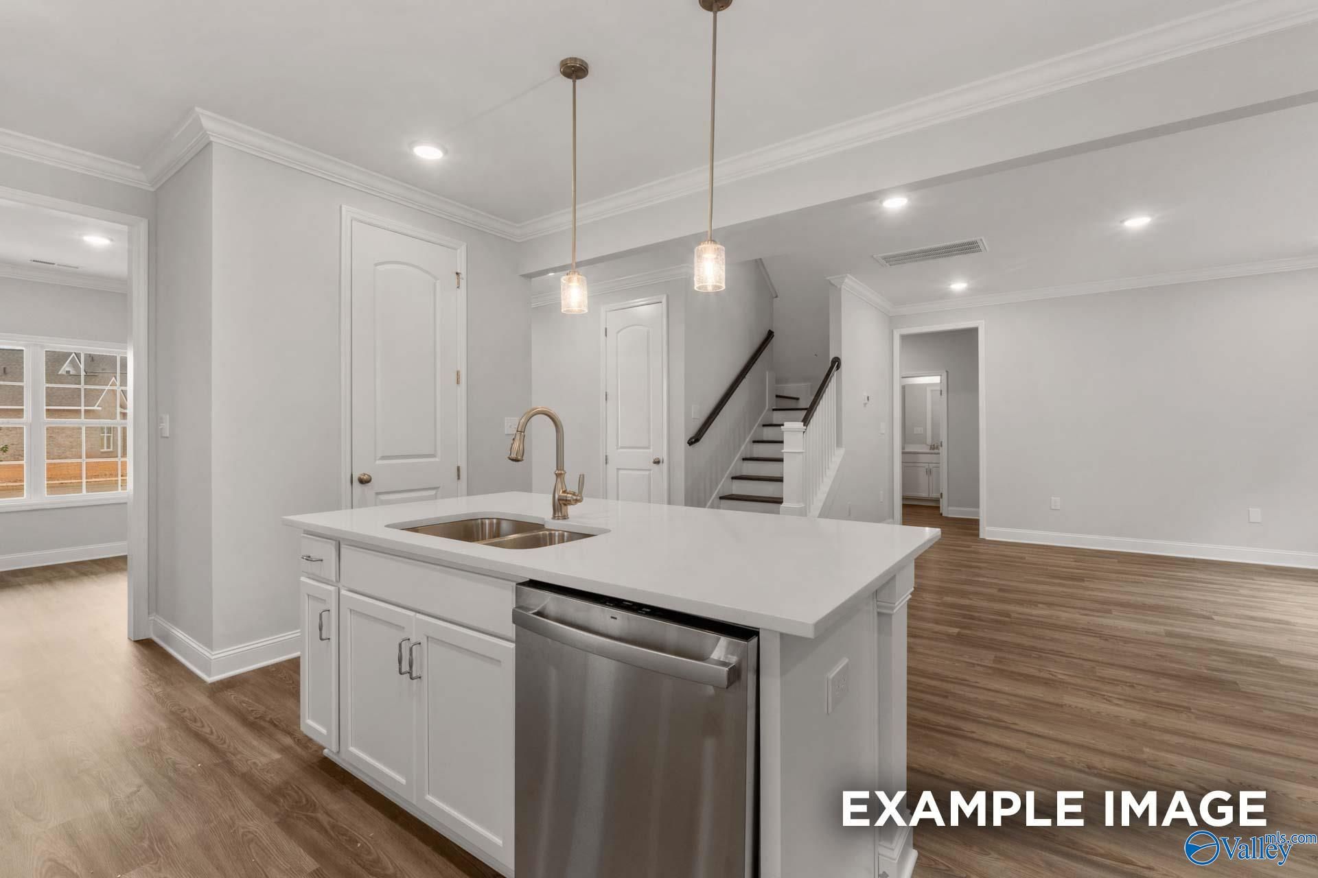 Modern white kitchen island with quartz countertop, gold faucet, stainless dishwasher, and open staircase in Davidson Homes The Shelby C, Arab, Alabama