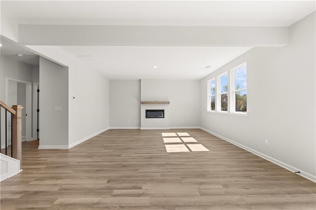 Spacious living room with hardwood floors, modern fireplace, and large sunny windows in The Hickory B by Davidson Homes, Winder, Georgia