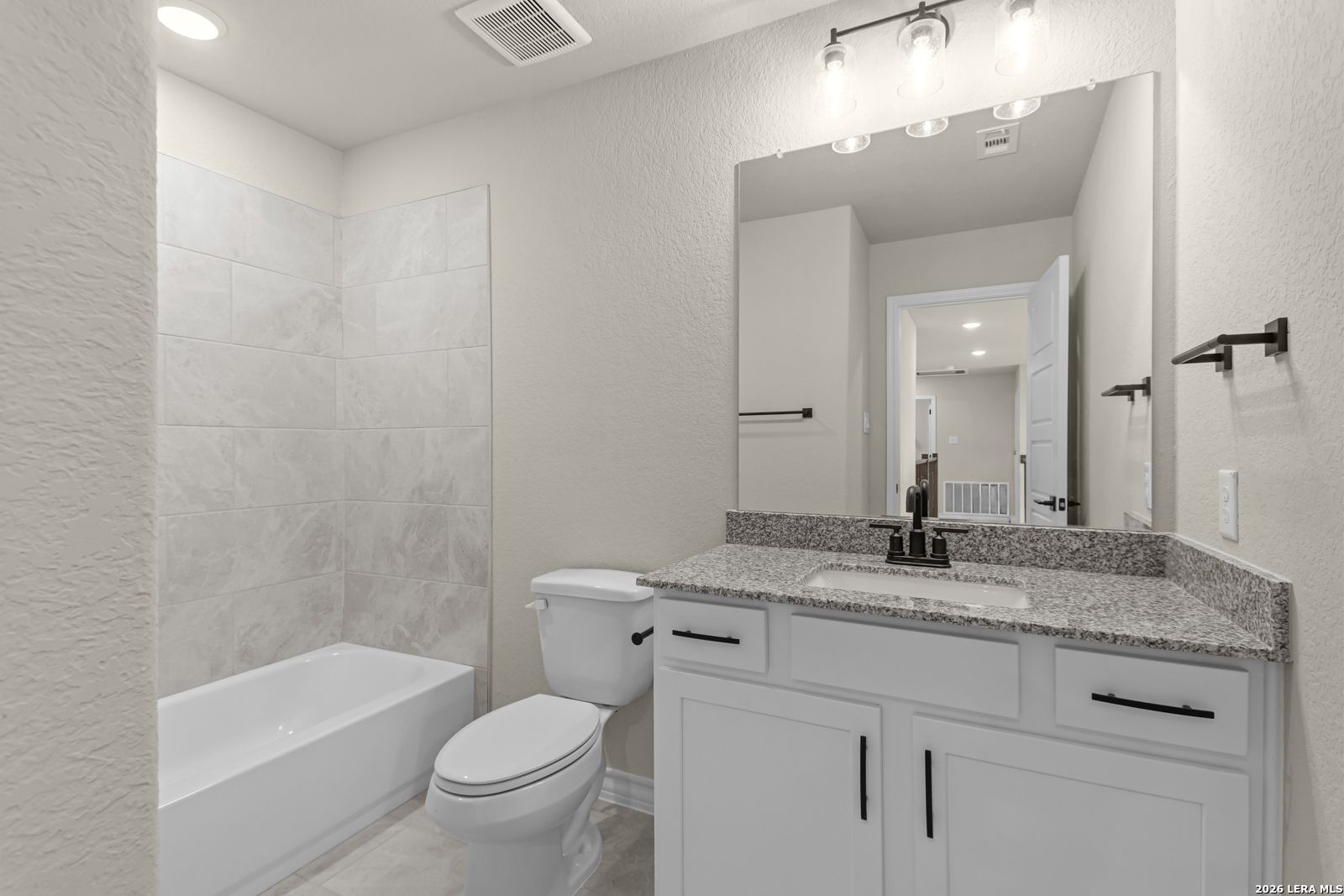 Modern bathroom with granite vanity and tile tub surround in The Danbury H floor plan at The Reserve at Potranco Oaks.