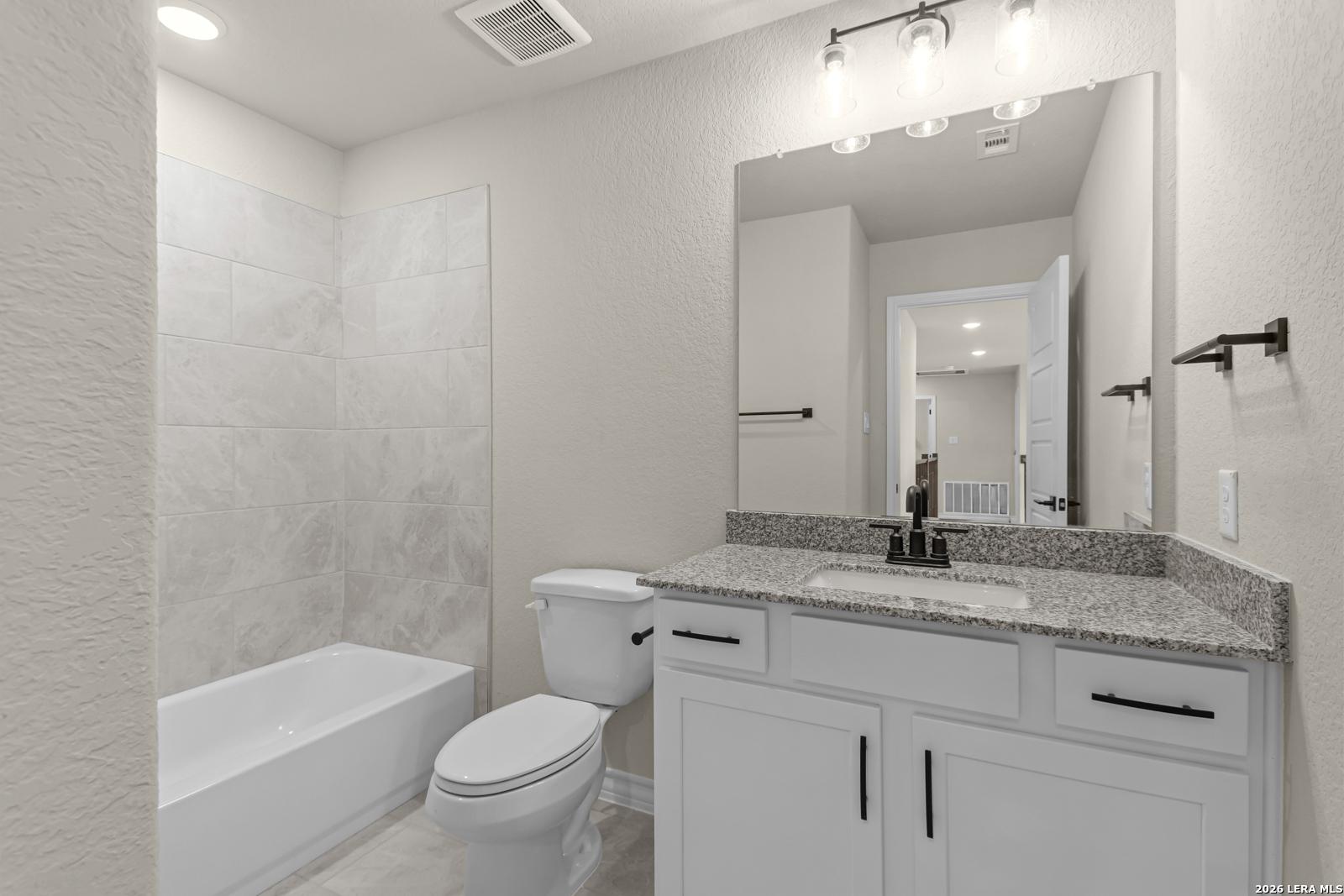 Modern bathroom with granite vanity and tile tub surround in The Danbury H floor plan at The Reserve at Potranco Oaks.