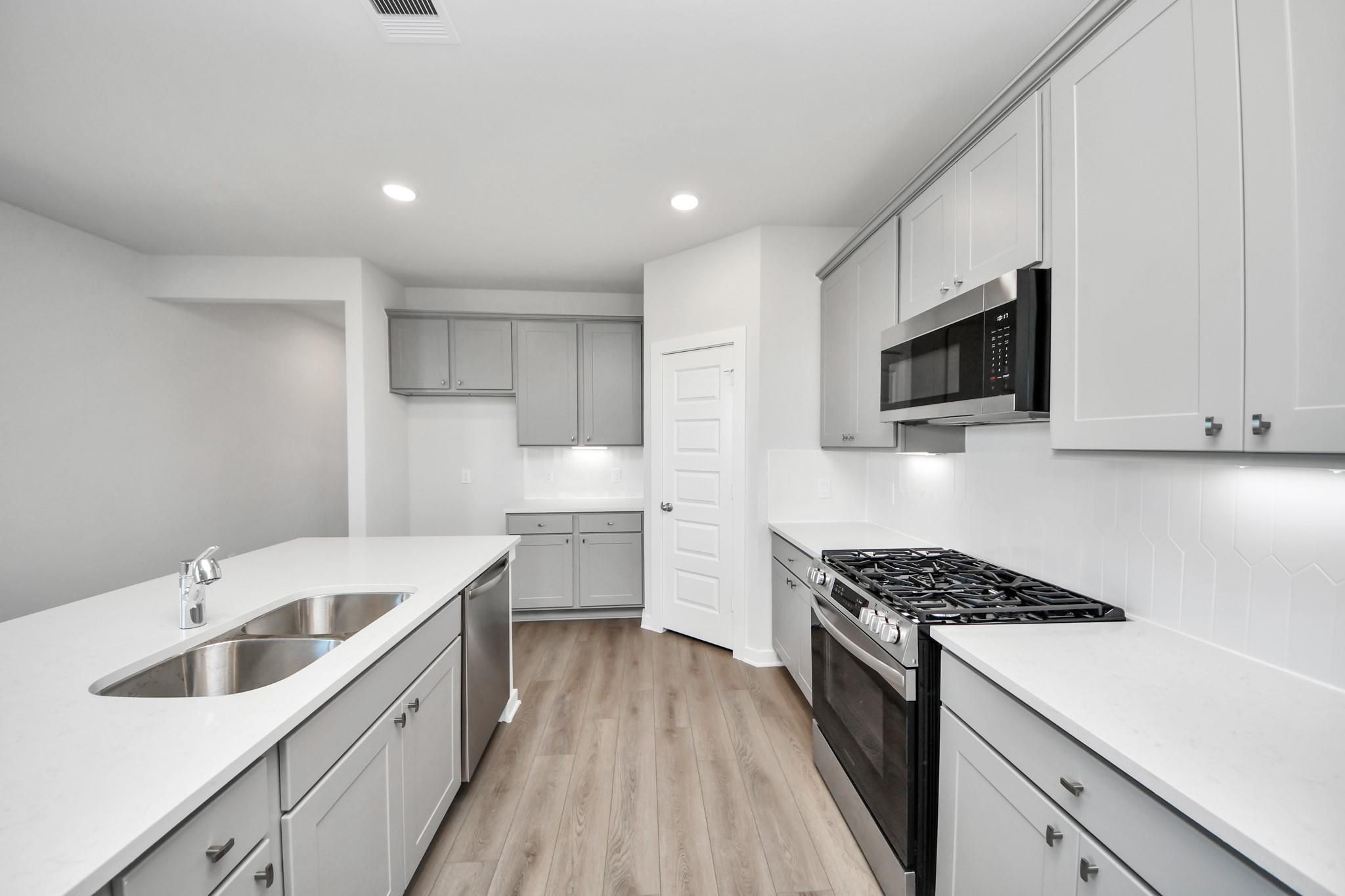 Modern kitchen with gray cabinets, quartz countertops, and stainless steel appliances in The Riviera A home at Emberly.