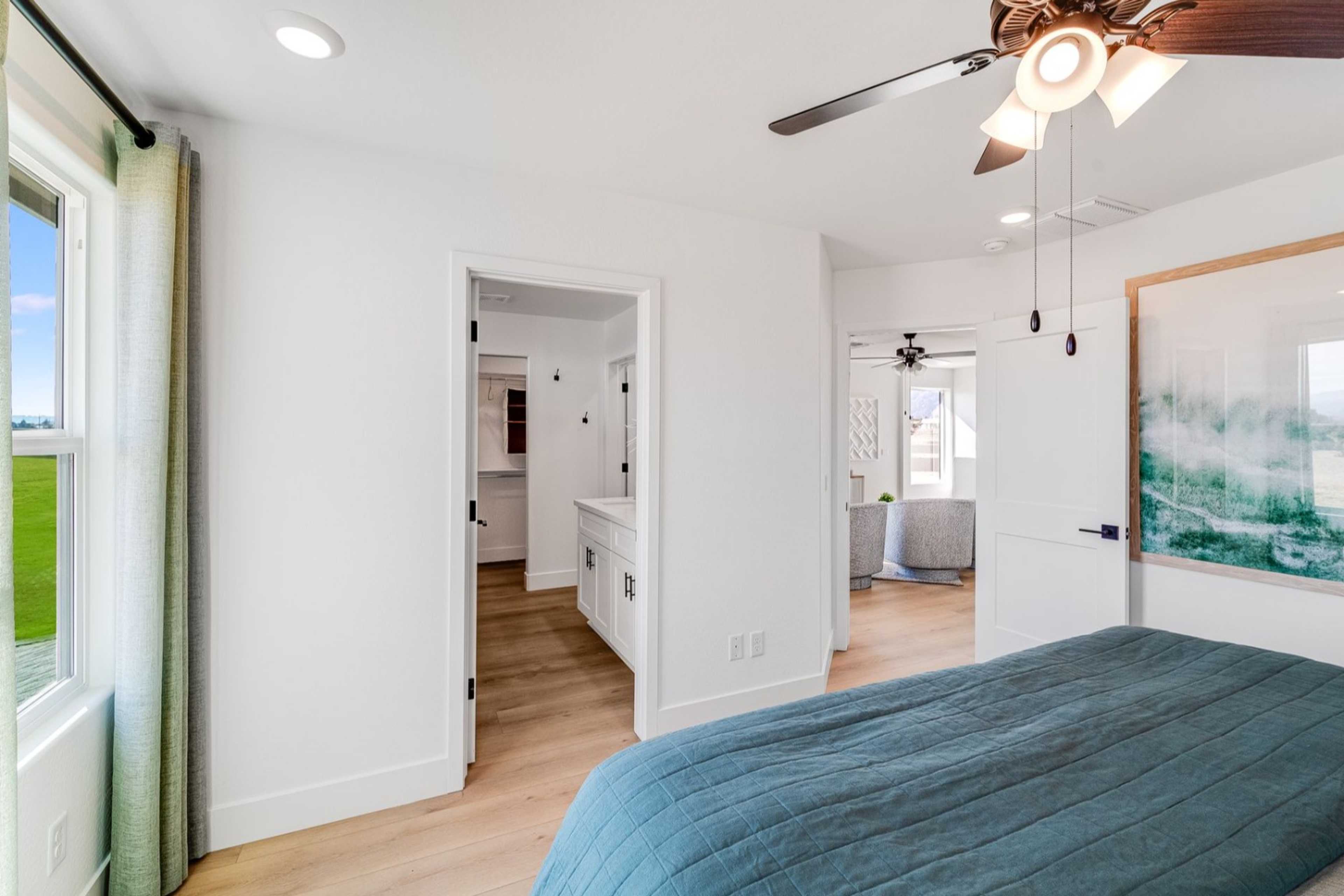 Spacious master bedroom in The Wilmington with king bed, ceiling fan, ensuite bath, and scenic window view