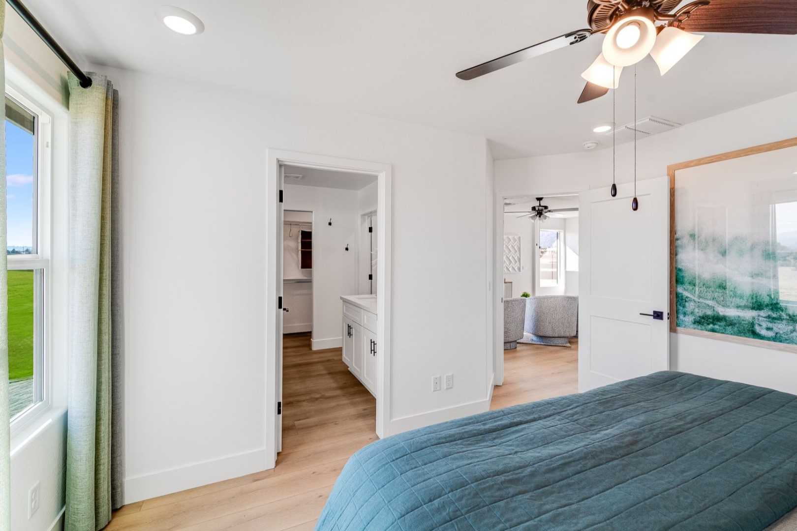 Spacious master bedroom in The Wilmington C with ceiling fan, large abstract artwork, en-suite bath, and scenic window view