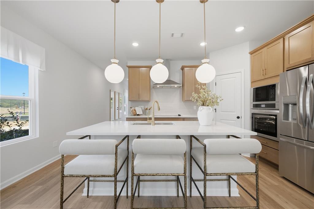 Kitchen island with white quartz countertop, gold pendant lights, and bar stools in Davidson Homes The Sinclair B, Cartersville, Georgia