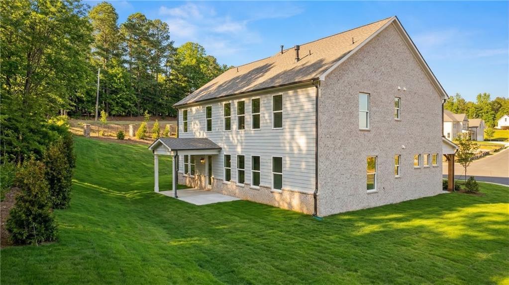 Two-story beige brick Danbury C home with covered porch, multiple windows, lush green lawn, and wooded backdrop in Melody Lakeside Estates, Buford, GA