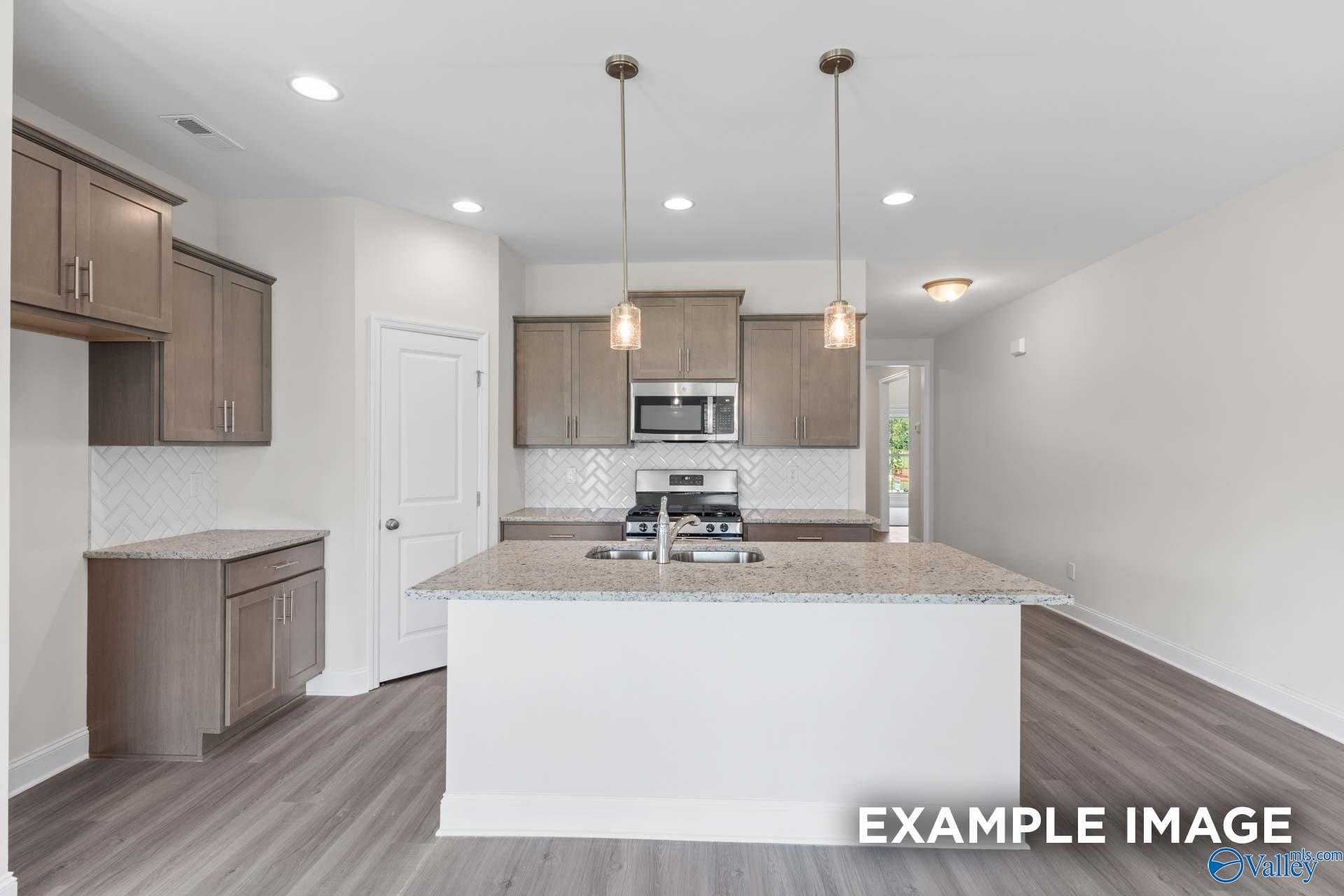 Modern kitchen with light wood cabinets, granite island sink, stainless appliances in The Daphne D 4-bedroom home, Arab, Alabama