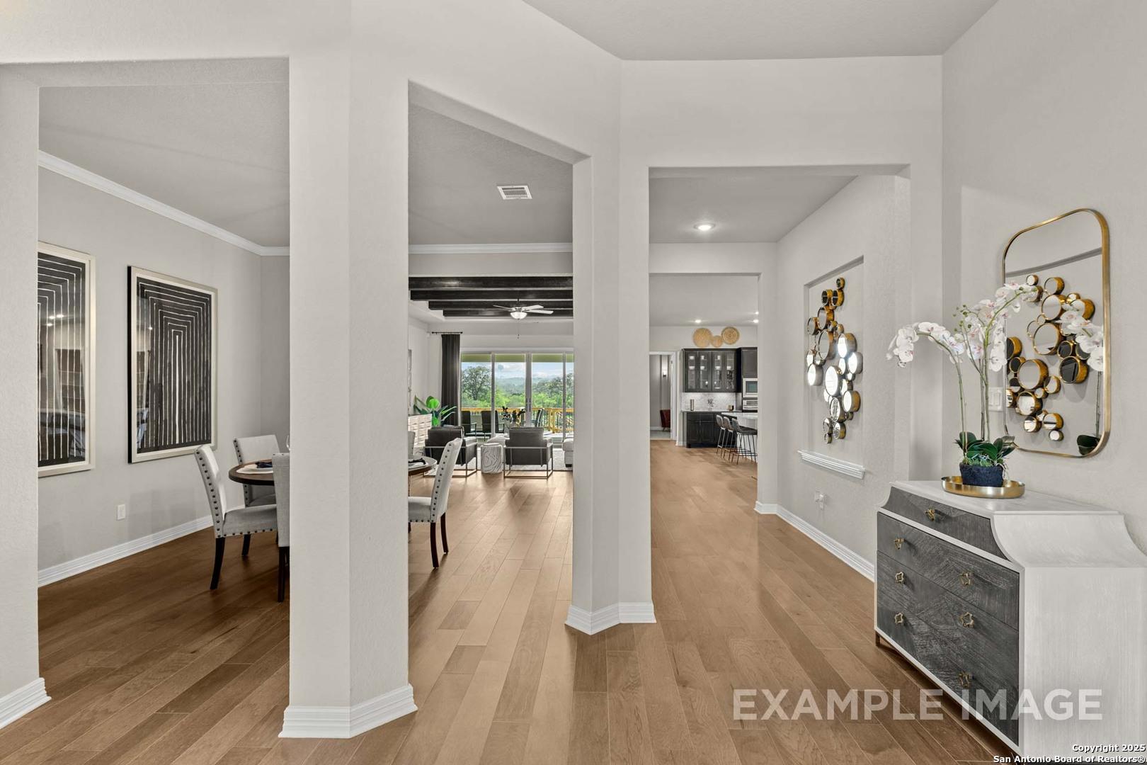 Open-concept dining area with hardwood floors, wooden table, chairs, and backyard view in Davidson Homes The Summerlin B, Castroville, Texas