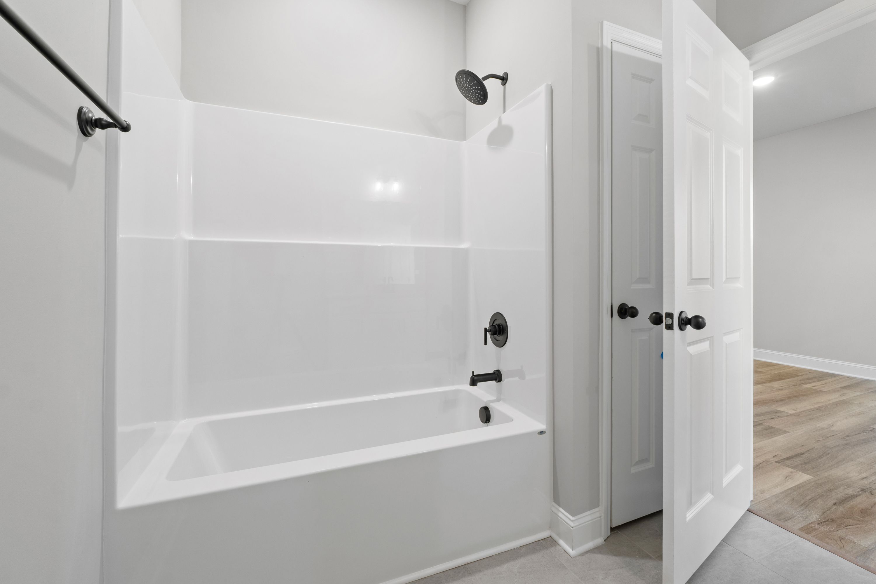 Spacious Valencia bathroom with white tub, glass shower enclosure, and open door to hallway in Davidson Homes design
