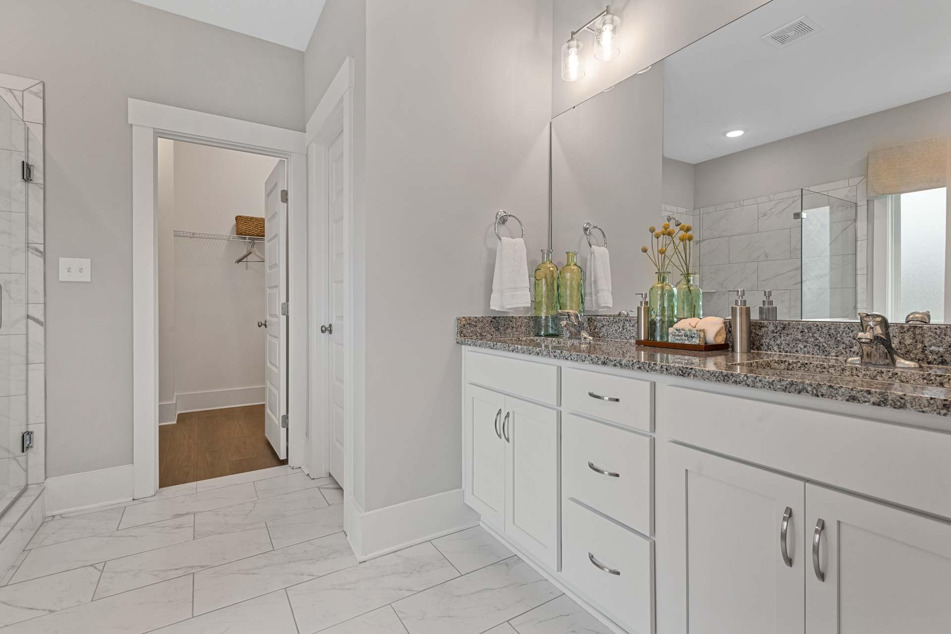 Spacious primary bathroom at Monteagle Cove in Owens Cross Roads AL with double vanity, granite counters, subway tile shower, and walk-in closet