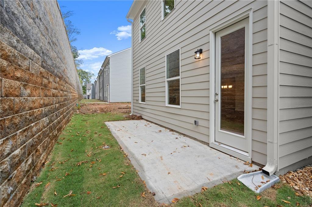 Side view of The Marion B two-story home with concrete patio, glass door, stone wall, and grassy yard in The Village at Shallowford, Kennesaw, Georgia