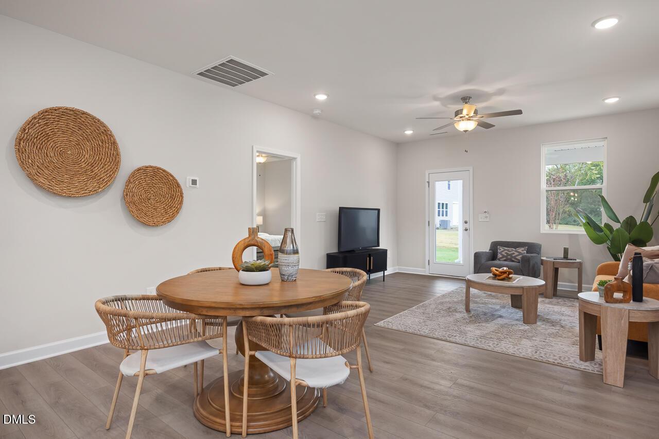 Open-concept living room with round wood dining table, woven wall art, TV stand, and sliding doors to backyard in The Carter C floor plan, Lillington, NC