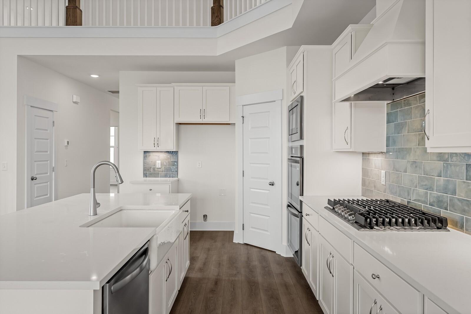 Modern kitchen with white cabinetry, quartz countertops, and blue tile backsplash in The Ridgeport D at Benders Cove.