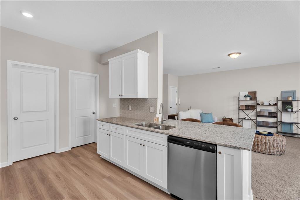 Modern open-concept kitchen with white shaker cabinets, quartz island, farmhouse sink, and stainless dishwasher in The Bartlett floor plan, Phenix City, Alabama