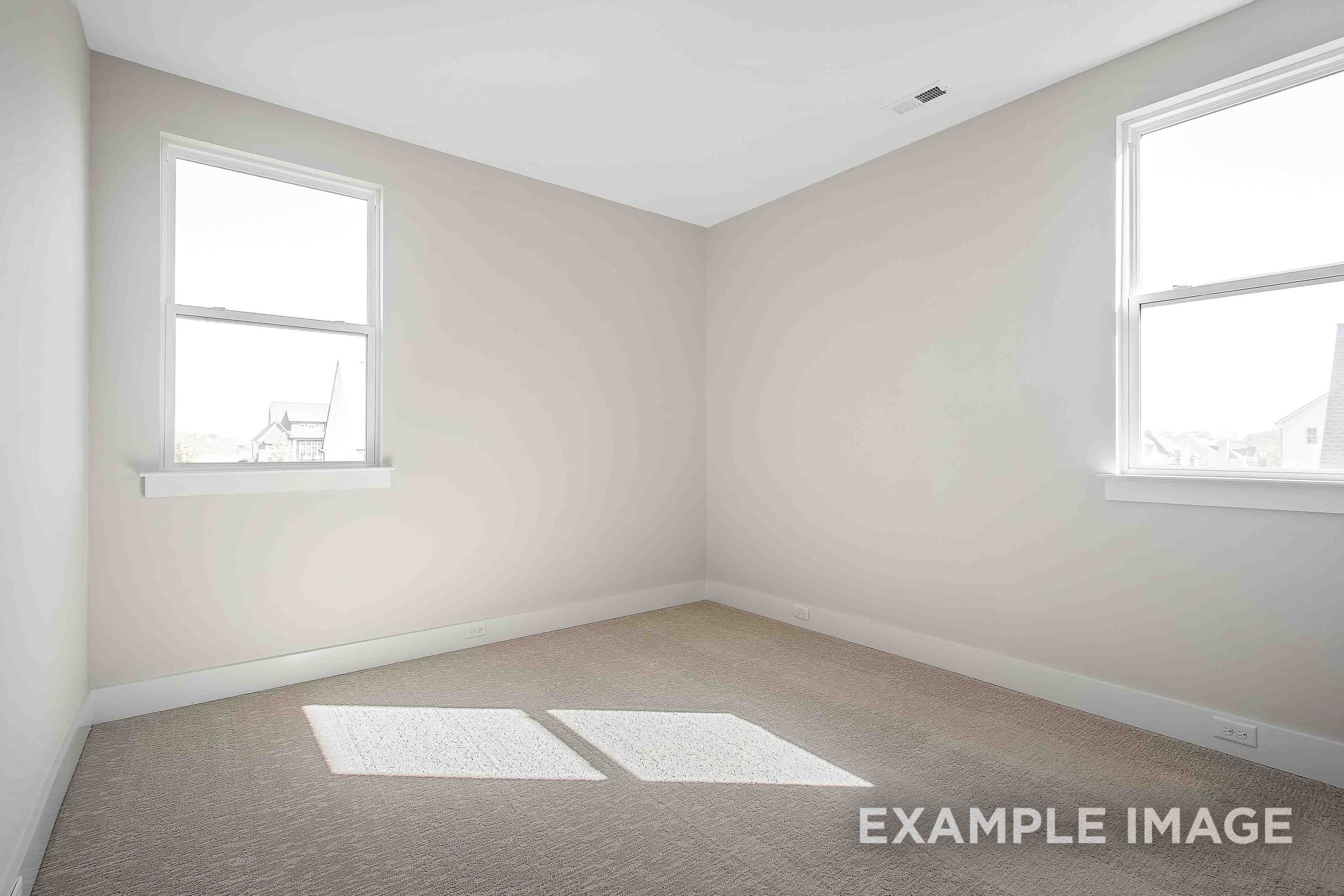 Spacious empty bedroom in The Alston A design with beige walls, carpet floor, and large windows streaming natural light
