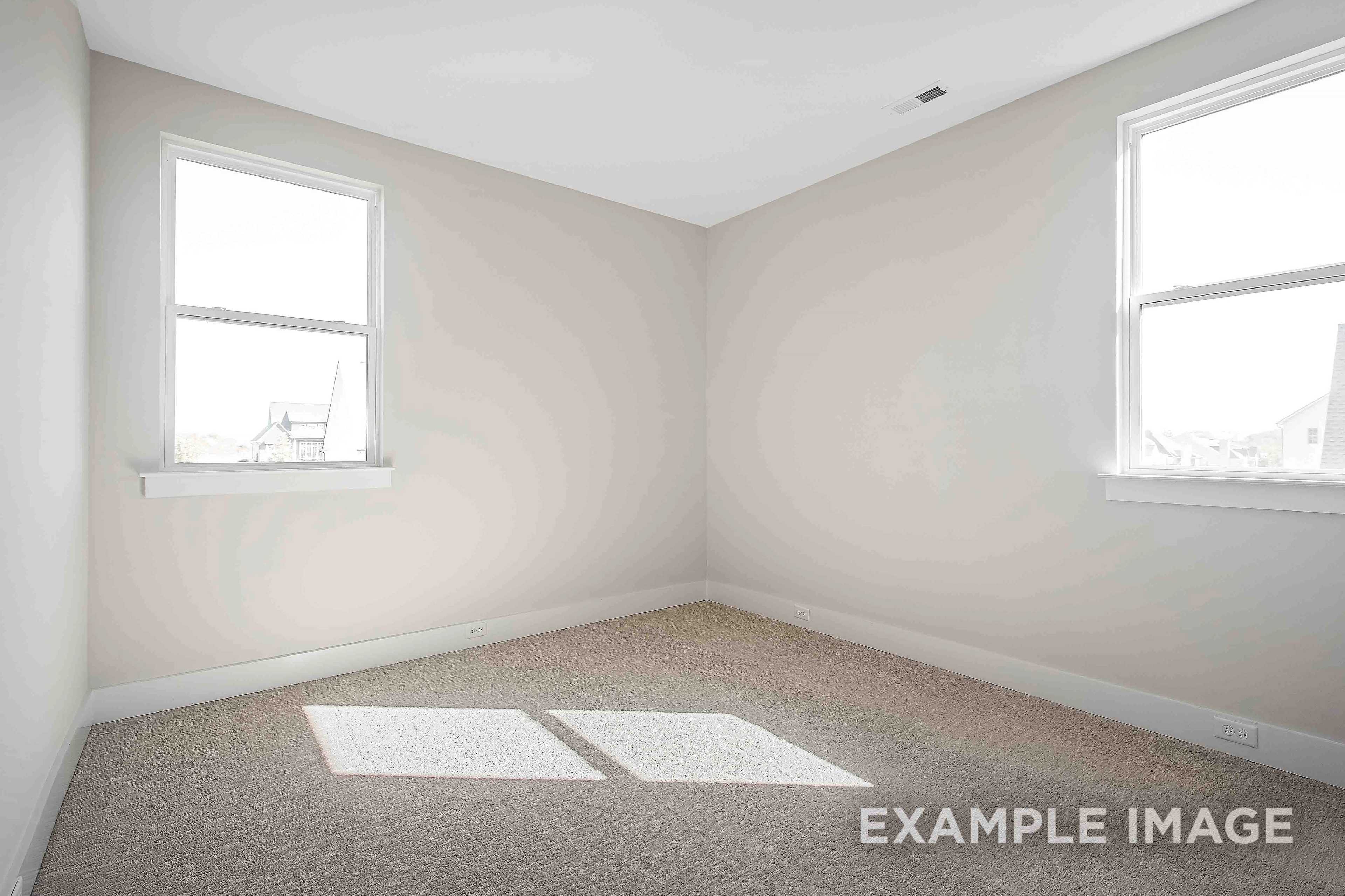 Spacious empty bedroom in The Alston A design with beige walls, carpet floor, and large windows streaming natural light