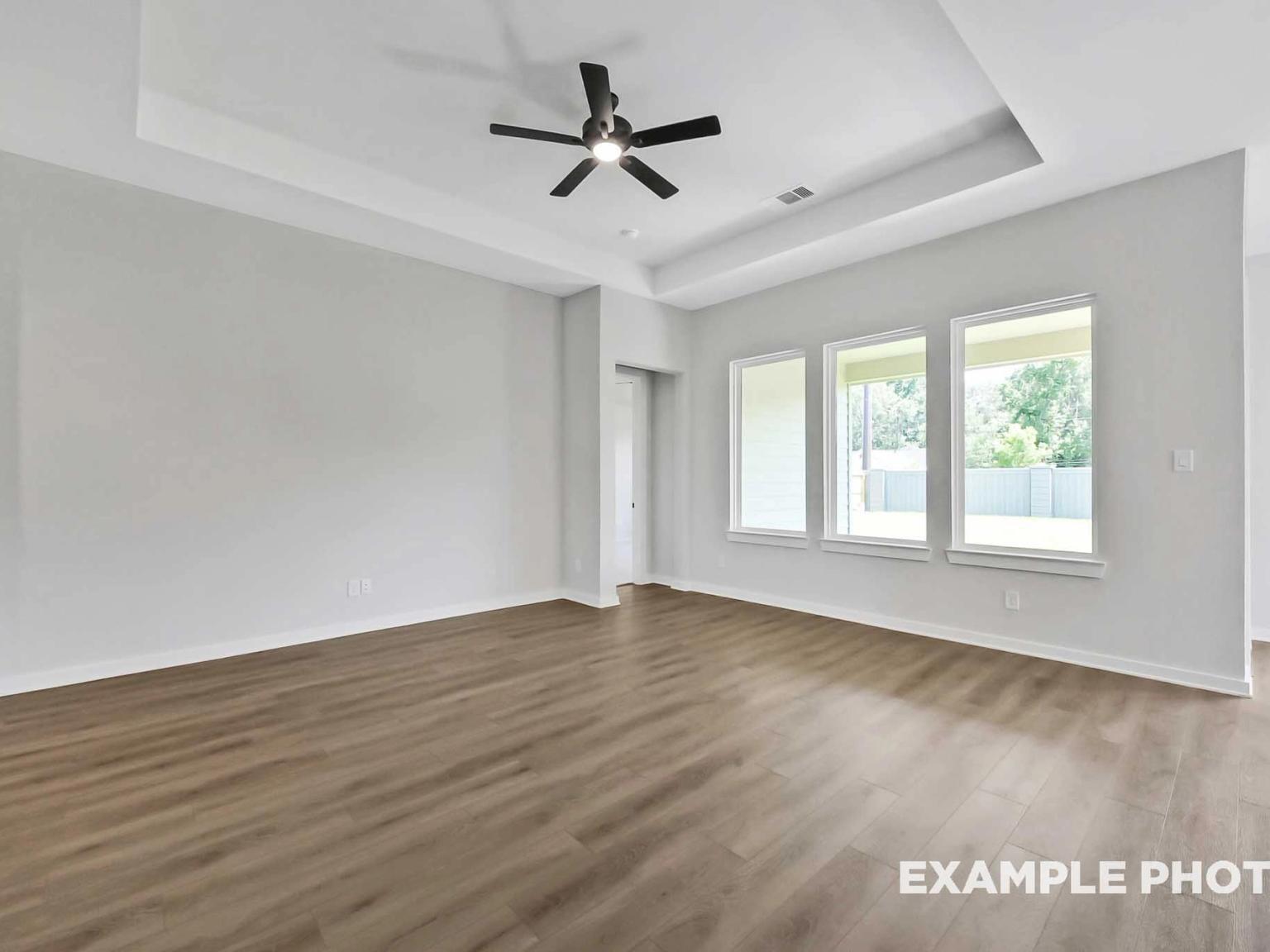 Bright living room with tray ceiling and wood flooring in The Sequoia C floor plan at Sundance Cove in Crosby, Texas.
