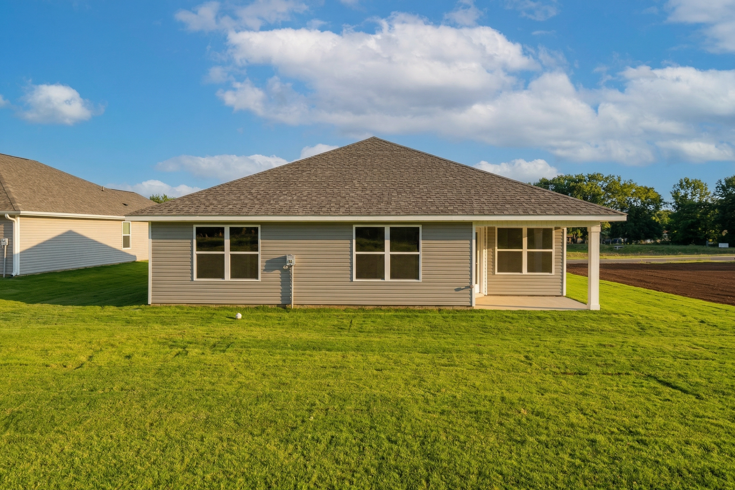 Exterior of The Daphne V single-story home with beige siding, gabled roof, covered porch, and lush green lawn in Meridianville