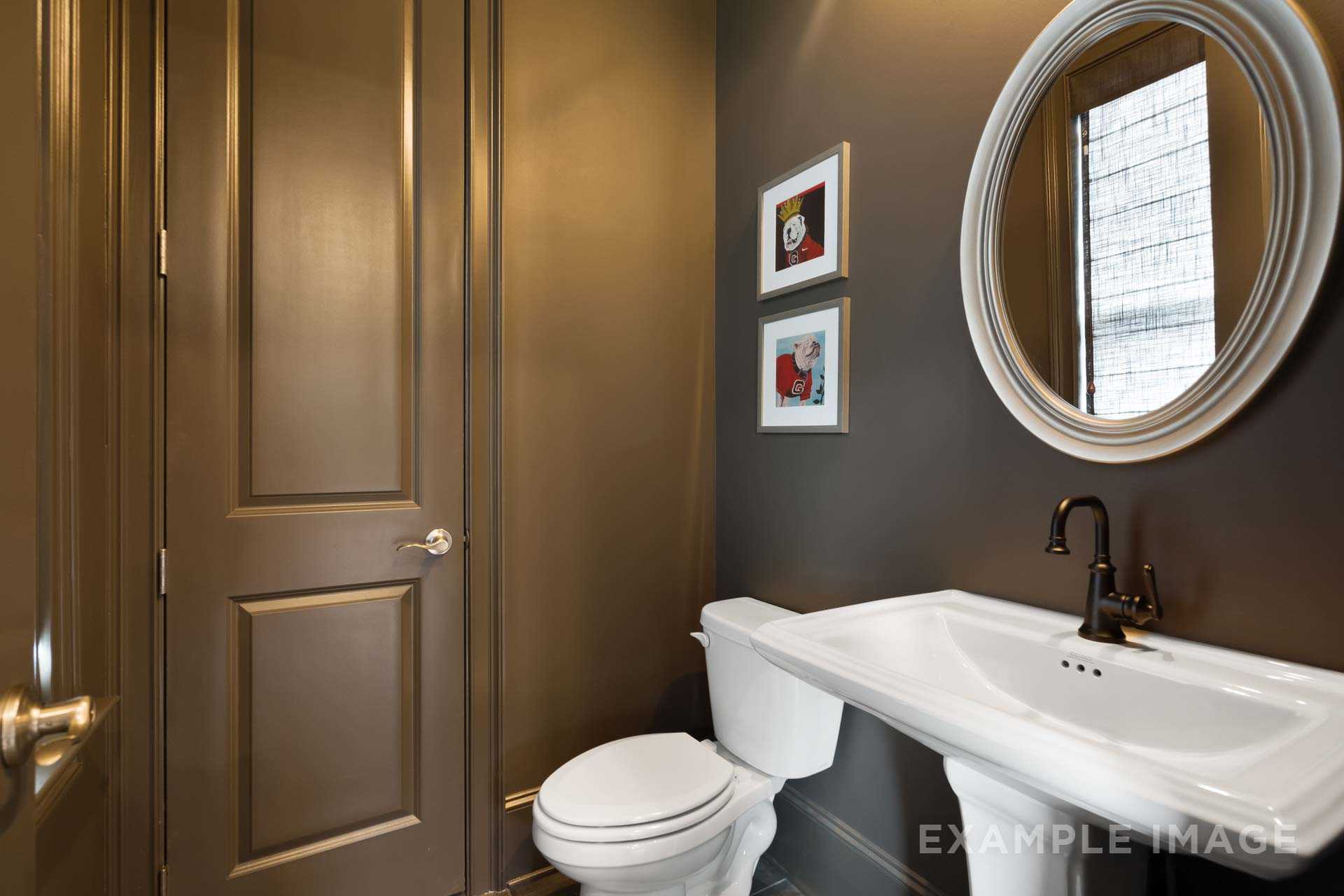 Elegant powder room in The Seaside Davidson Homes design featuring round mirror, pedestal sink, and brass faucet