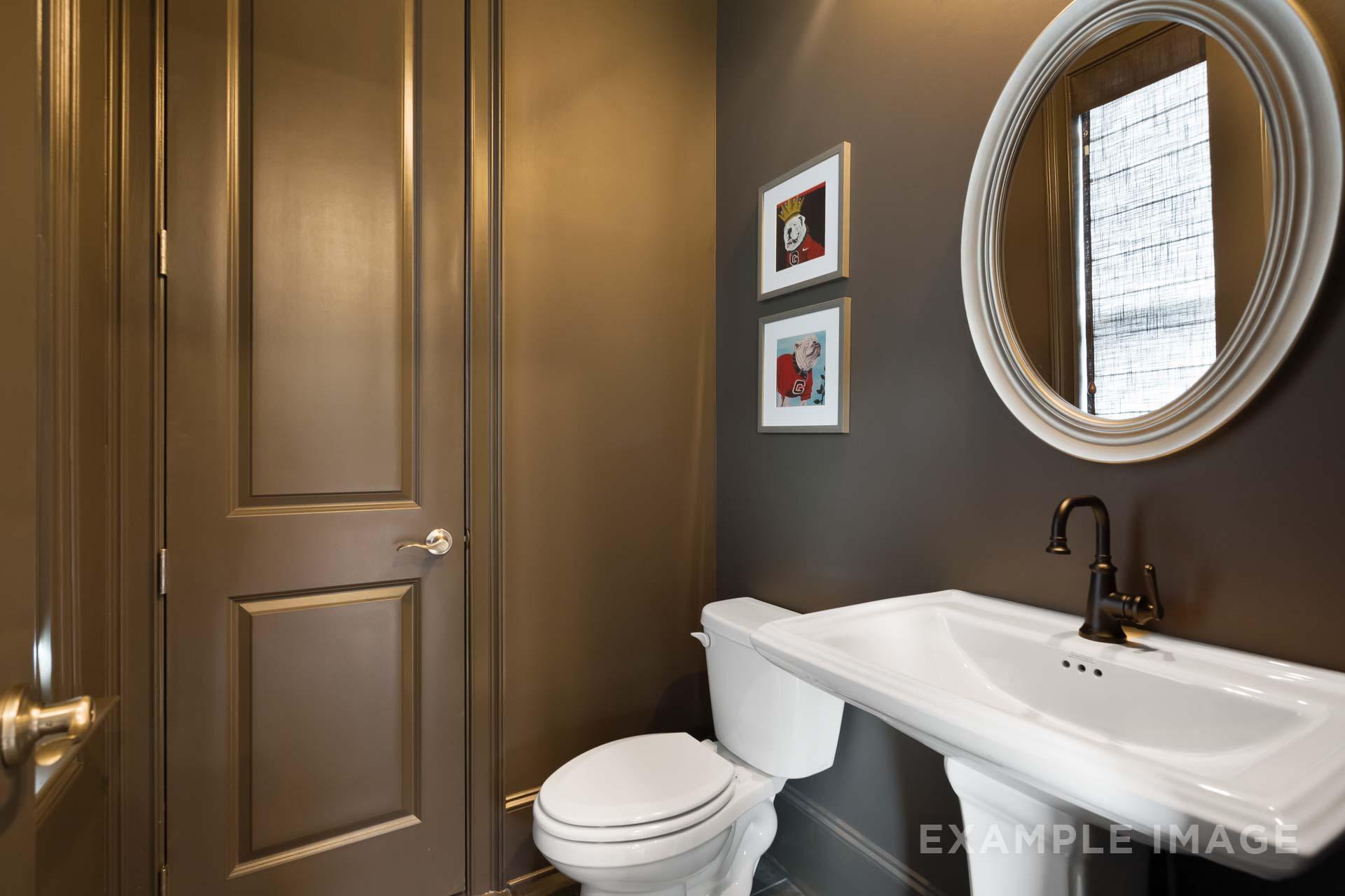 Stylish powder room in The Seaside C with wooden door, round mirror, vanity sink, and toilet