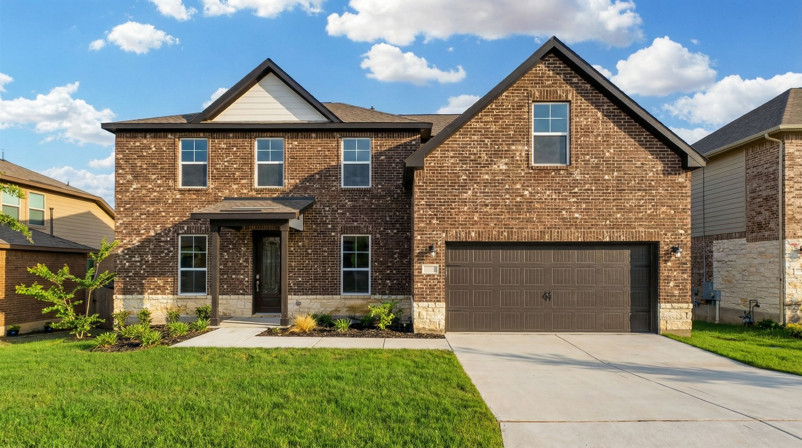 Brick two-story home exterior in Ladera San Antonio TX by Davidson Homes with covered porch, garage, and lush landscaping