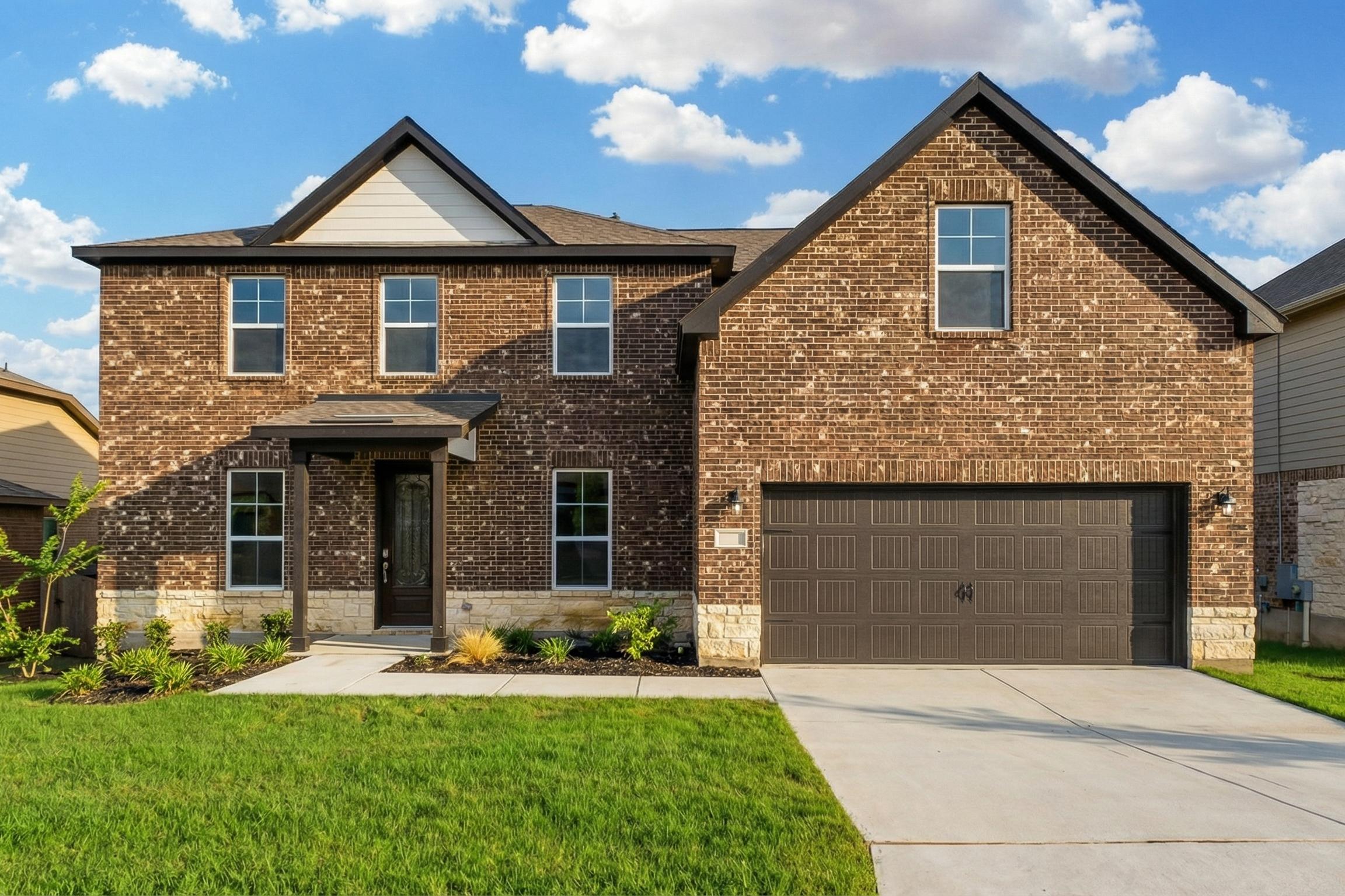 Brick two-story home exterior in Ladera San Antonio TX by Davidson Homes with covered porch, garage, and lush landscaping