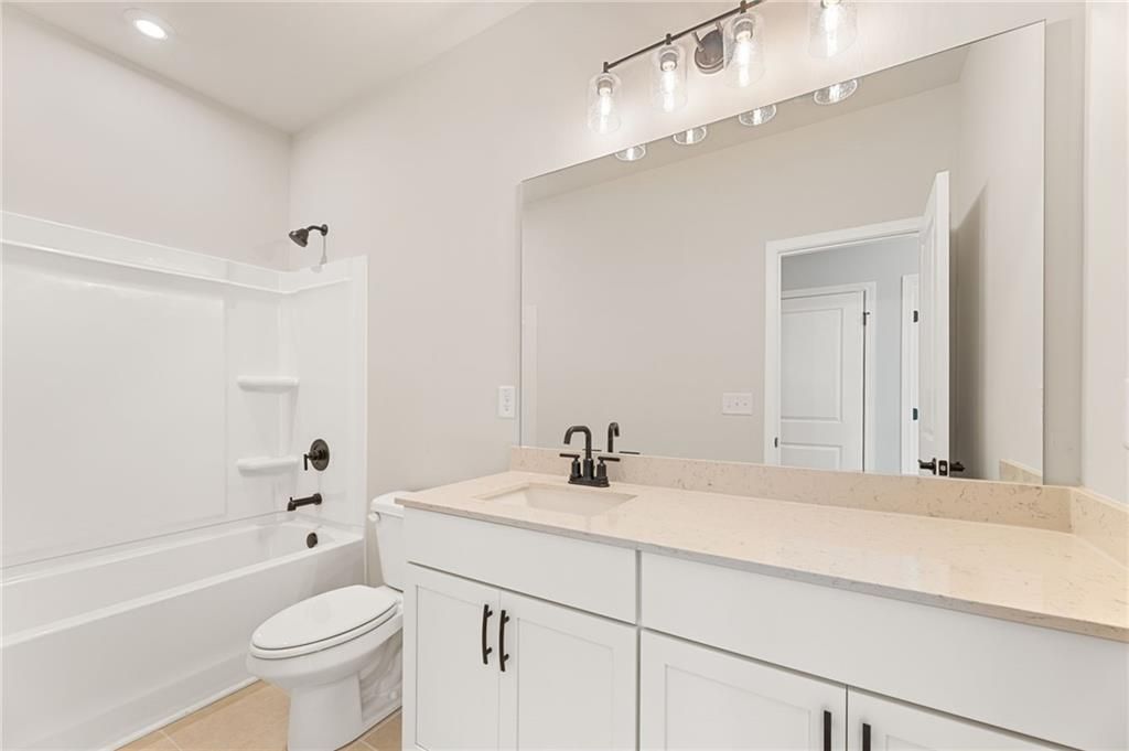 Modern bathroom featuring white tub, toilet, double vanity, and large mirror in Davidson Homes The Glenwood C, Loganville, GA