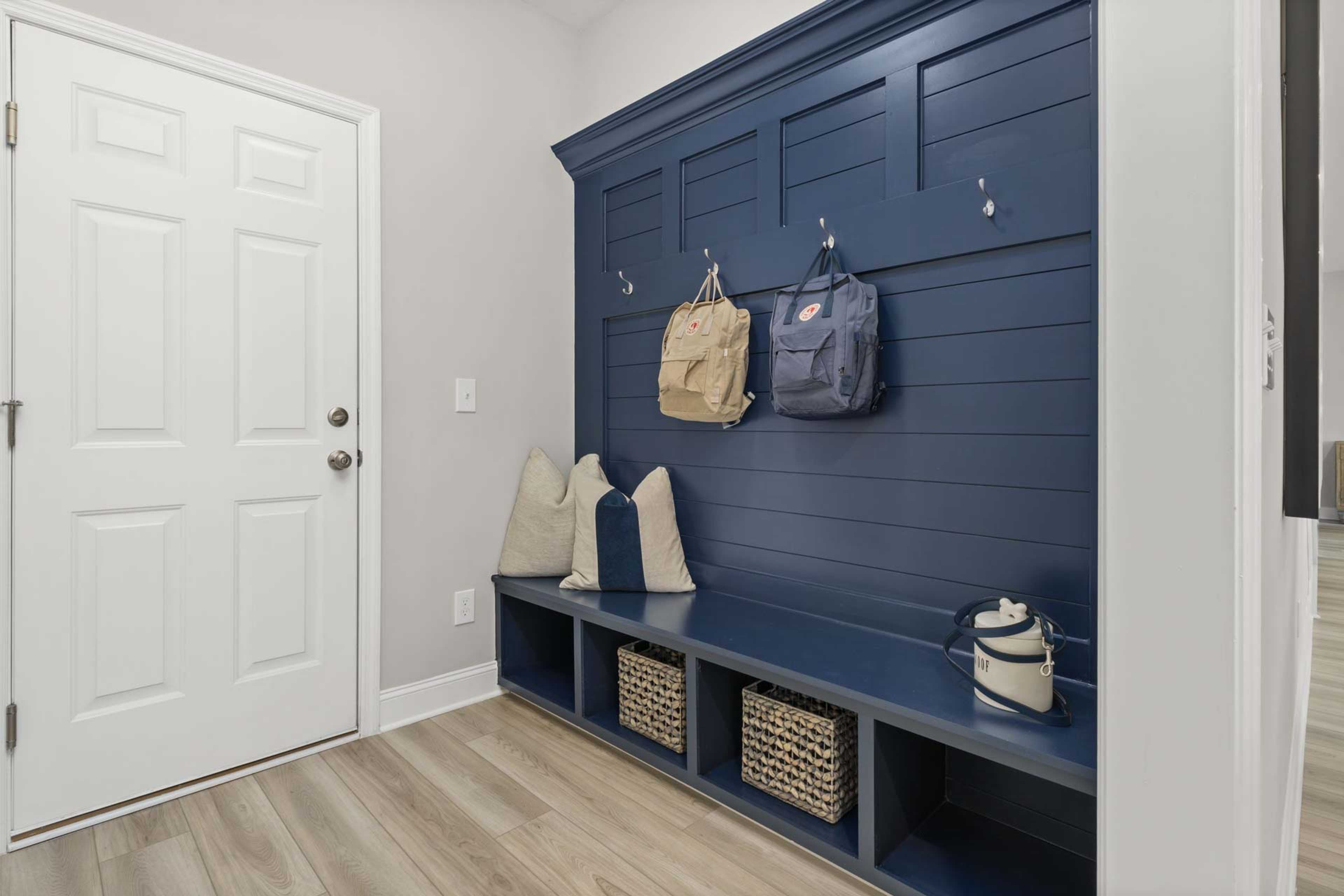 Navy blue shiplap entryway bench with hooks, backpacks, pillows, and wicker storage at Creek Grove in New Market, Alabama