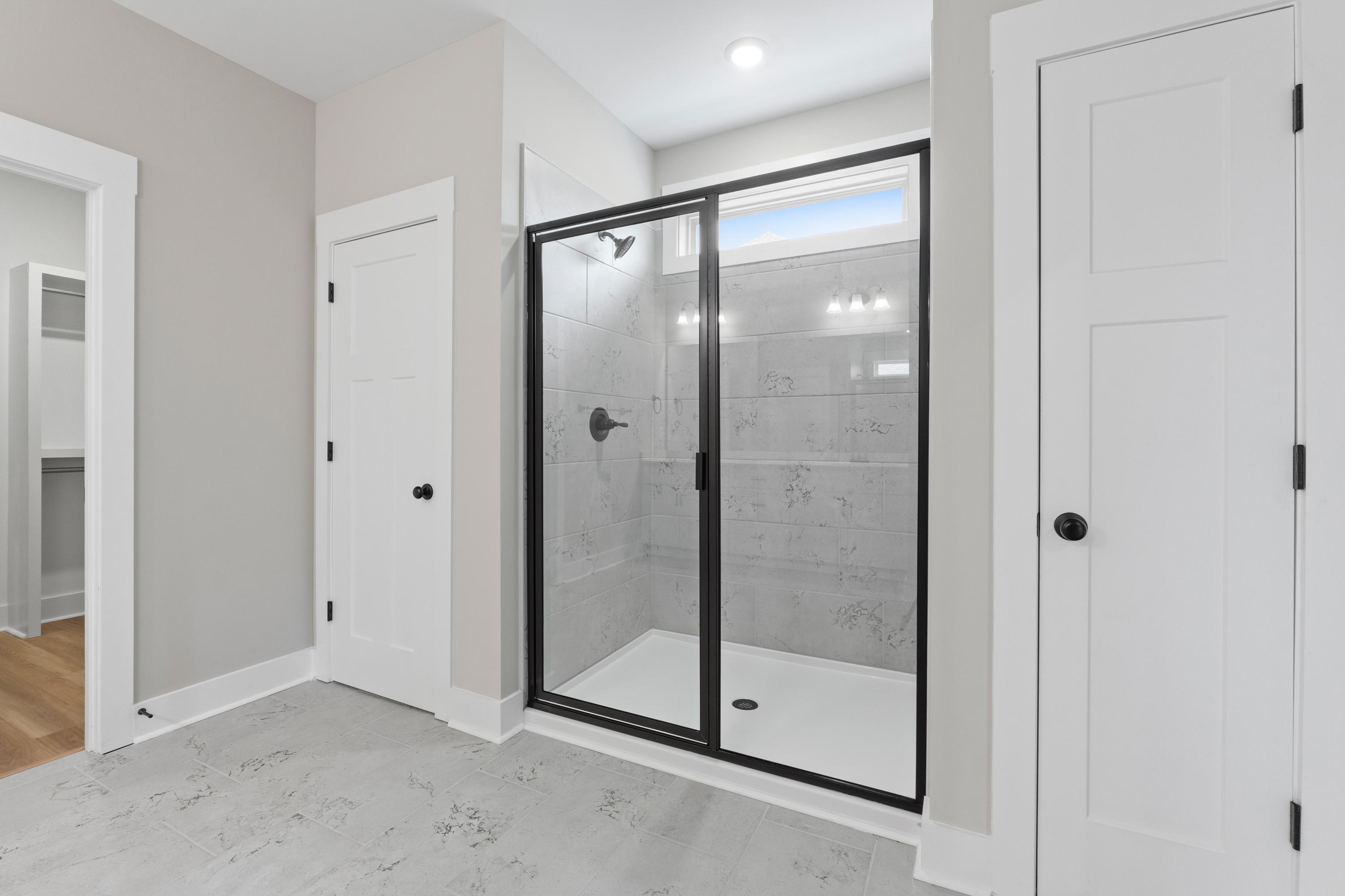 Spacious master bathroom in The Oxford with frameless glass shower, subway tile walls, and modern black fixtures